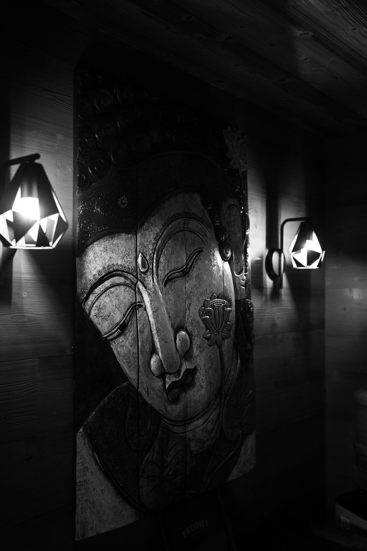 Black and white photo of ornate Buddha face carving illuminated by geometric wall lamps. Mallorca wedding photographer and filmmaker.