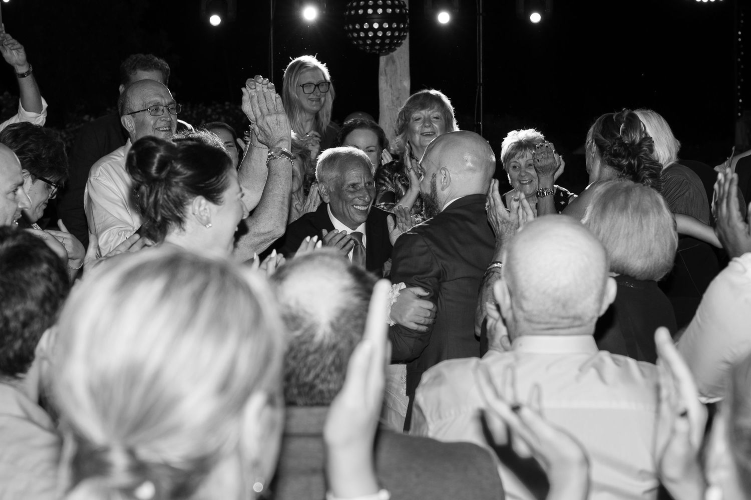 Black and white photo of a cheering crowd clapping and celebrating at an event under a disco ball.