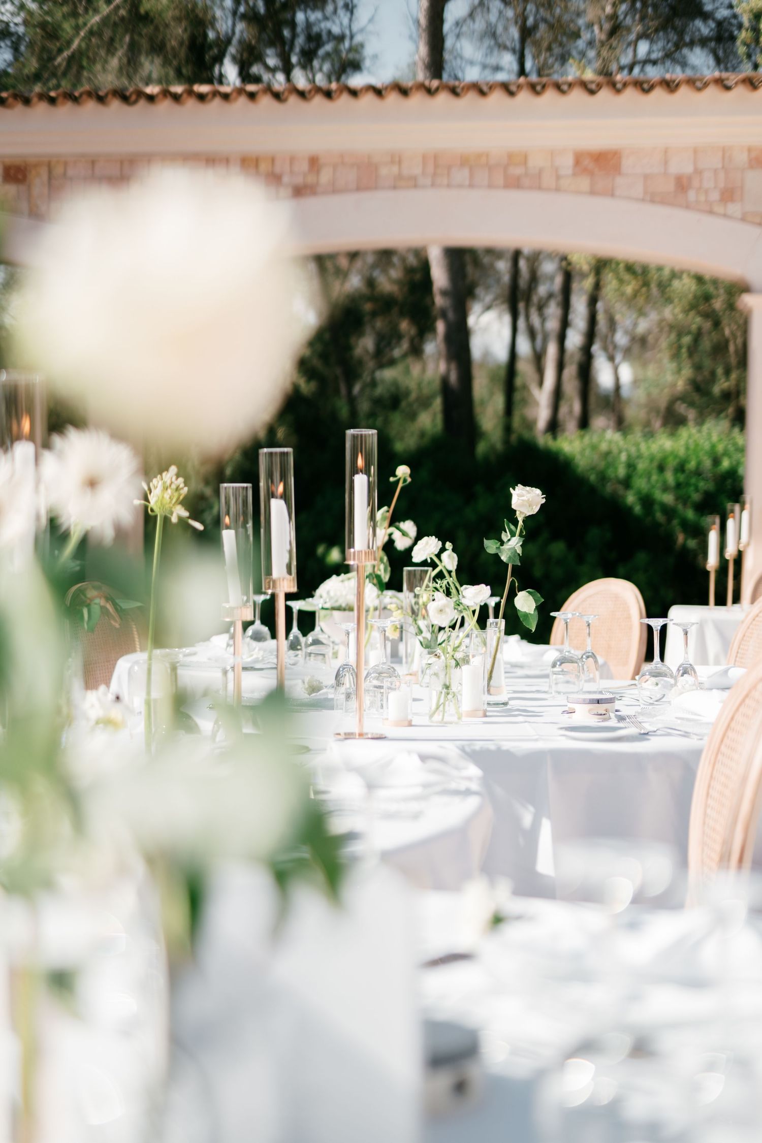 Elegant outdoor wedding reception table set with white linens, gold candle holders, and white floral arrangements in Mallorca.