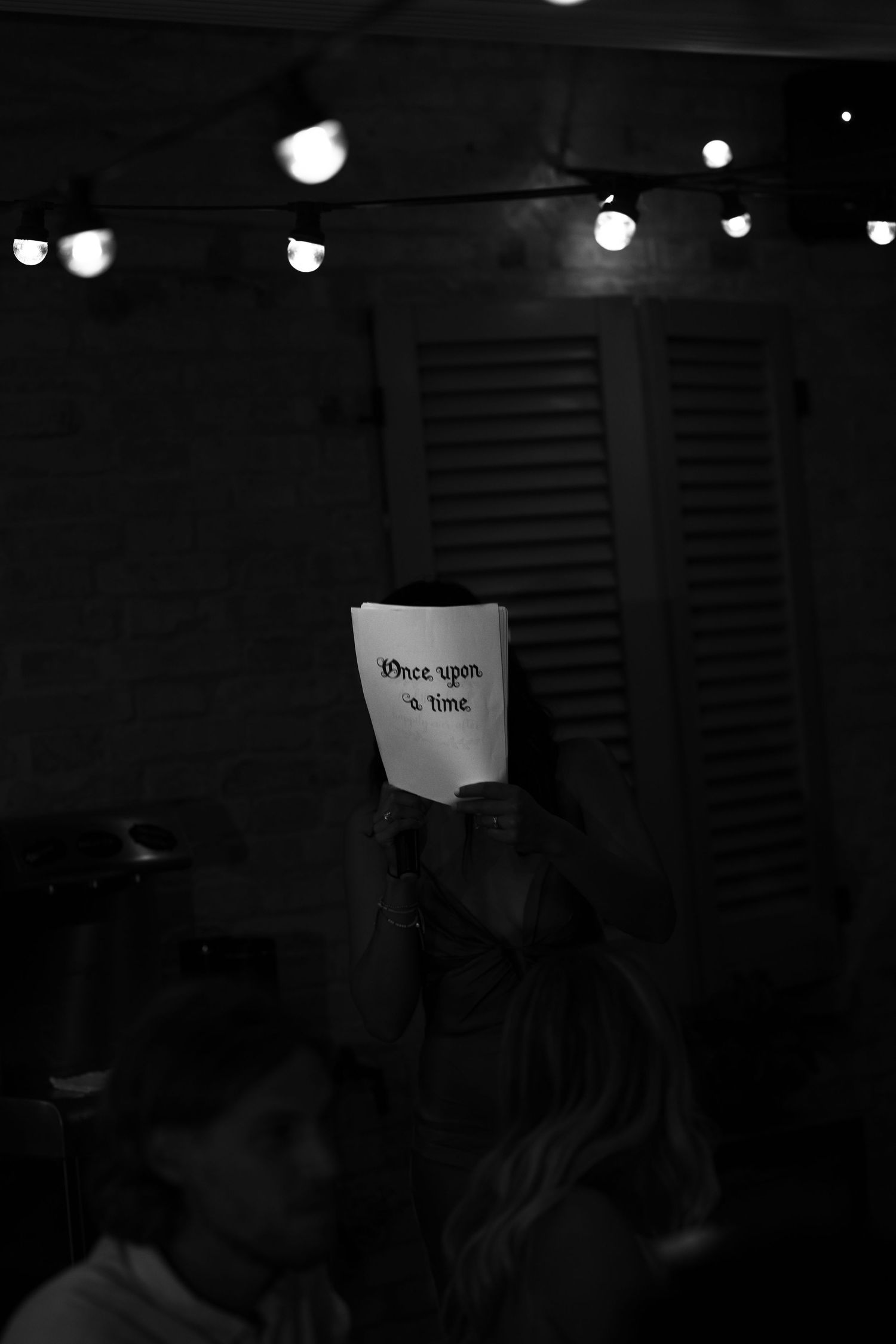 Person holding a paper sign reading Once upon a time, with string lights glowing in dark background.