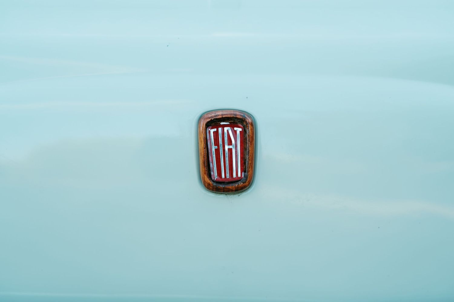 Close-up of a red and chrome Fiat badge emblem on the hood of a vintage mint green car.