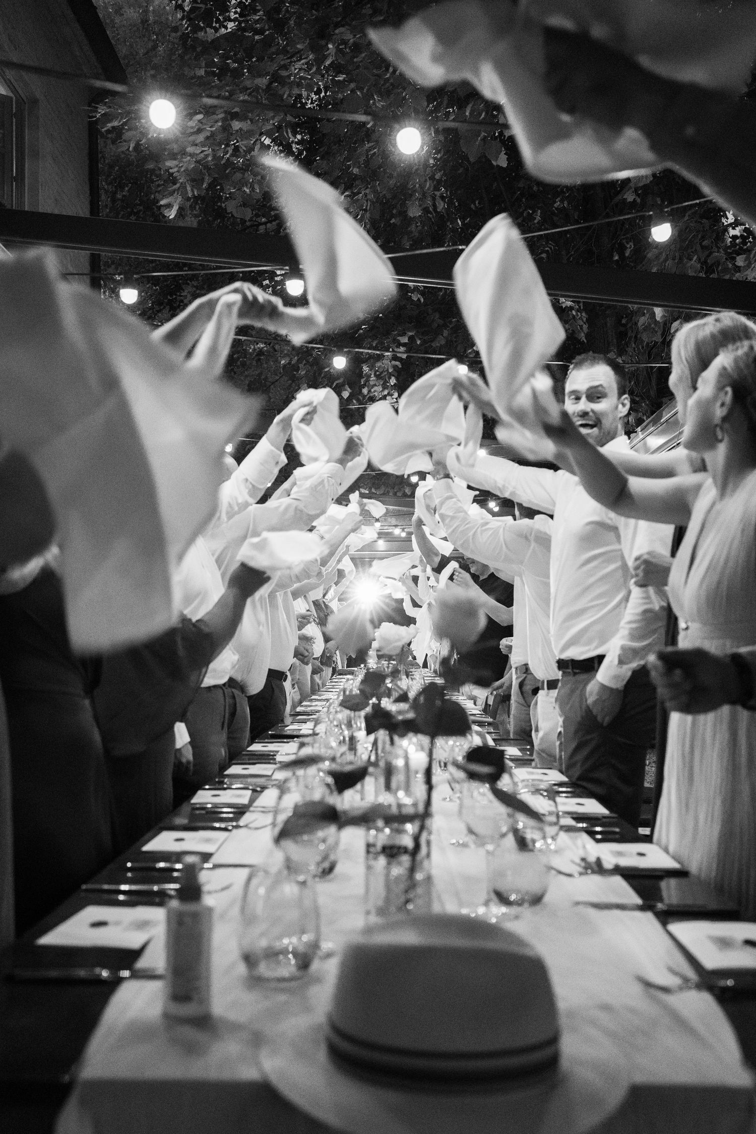 Guests wave white napkins in celebration at a festive outdoor wedding reception dinner.