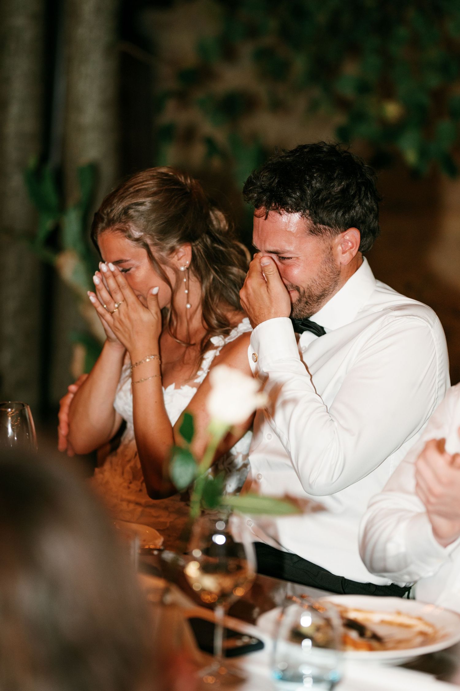Bride and groom crying tears of joy during wedding reception speeches at elegant dinner table.