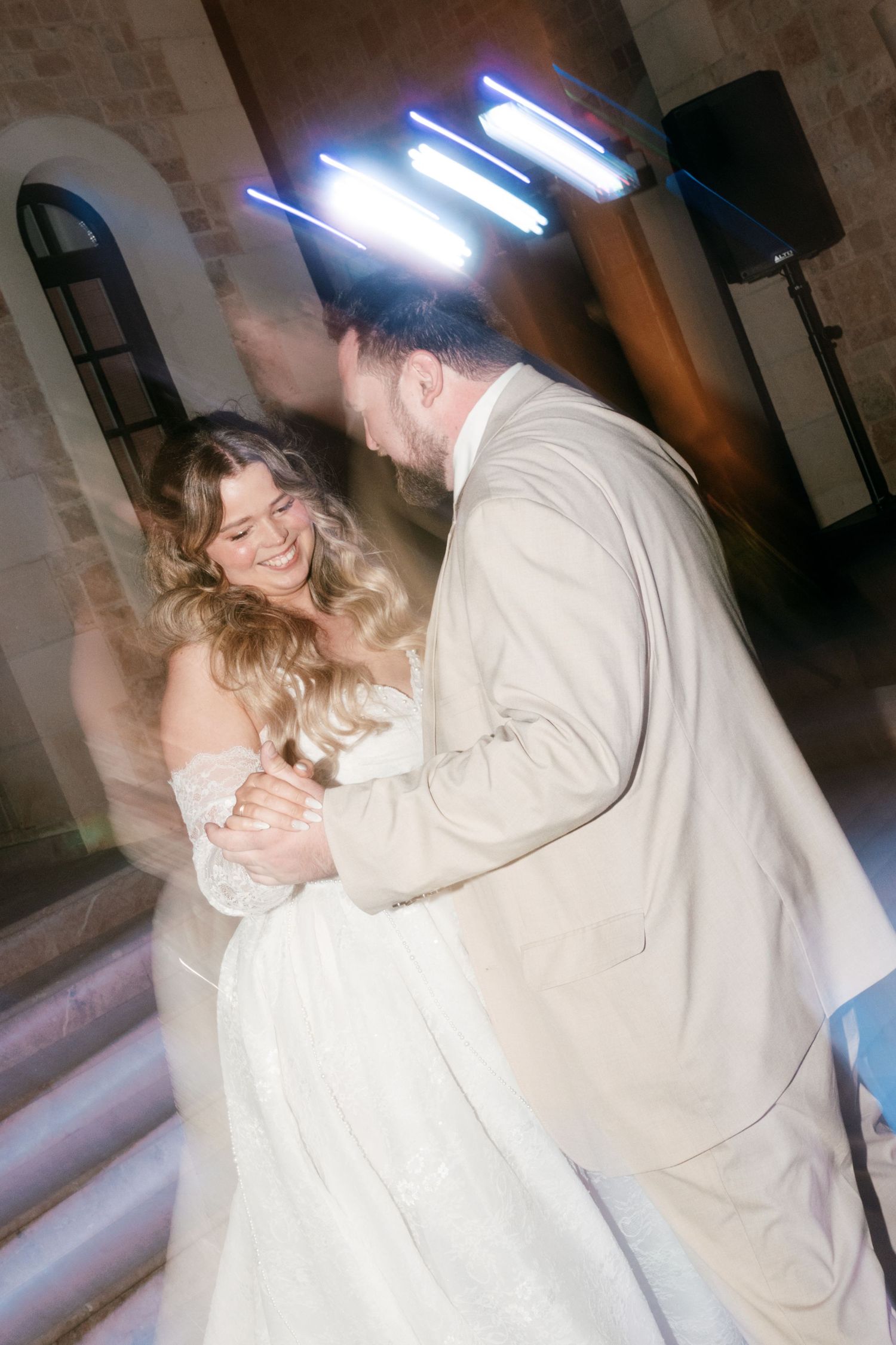 A bride in a white off-shoulder gown shares a first dance with her groom in a beige suit at their wedding reception in Mallorca.