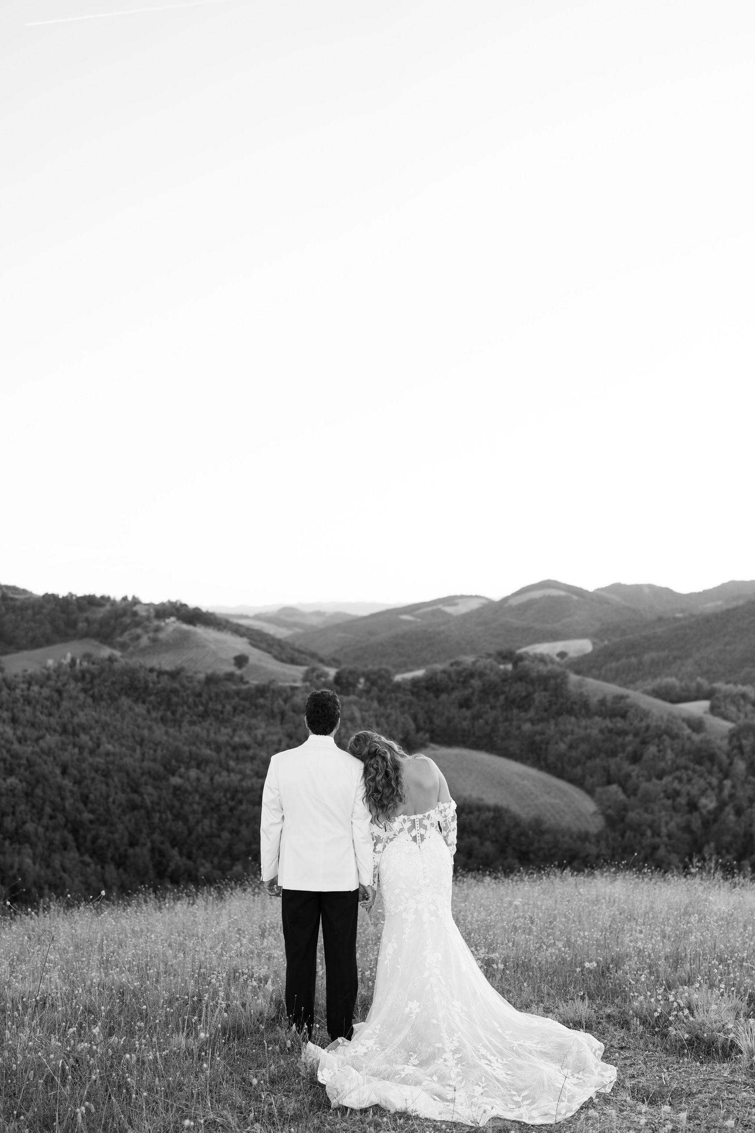 Black and white photo of bride and groom overlooking rolling hills landscape.