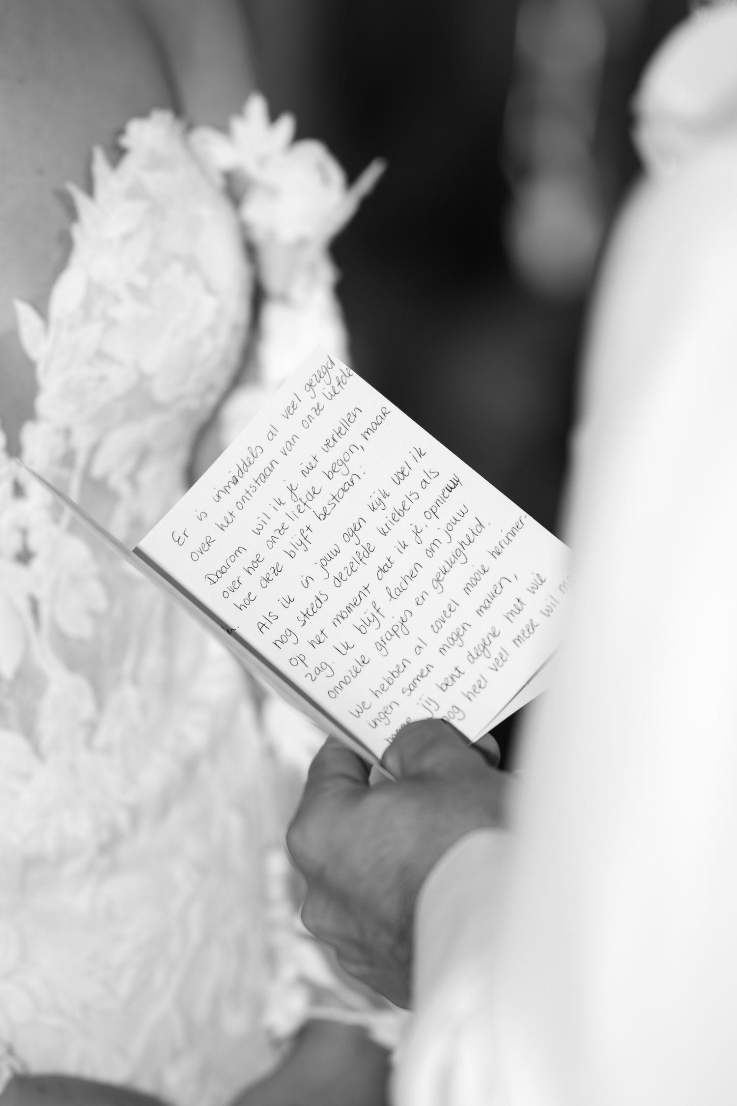 Black and white photo of a groom holding handwritten wedding vows on a card during a ceremony.