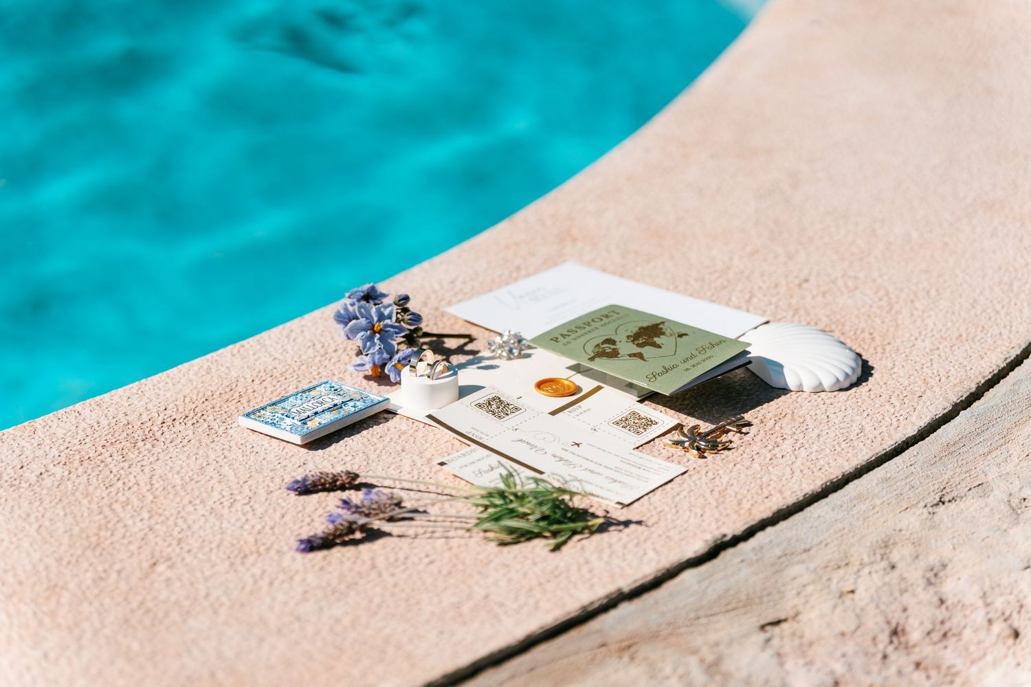 Lavender sprigs and botanical cards arranged by a turquoise swimming pool on a sunny day.