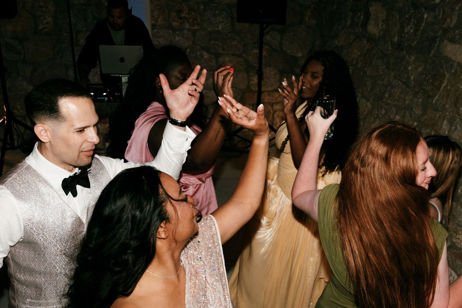 Wedding guests dancing joyfully at a lively reception party in a rustic stone venue.