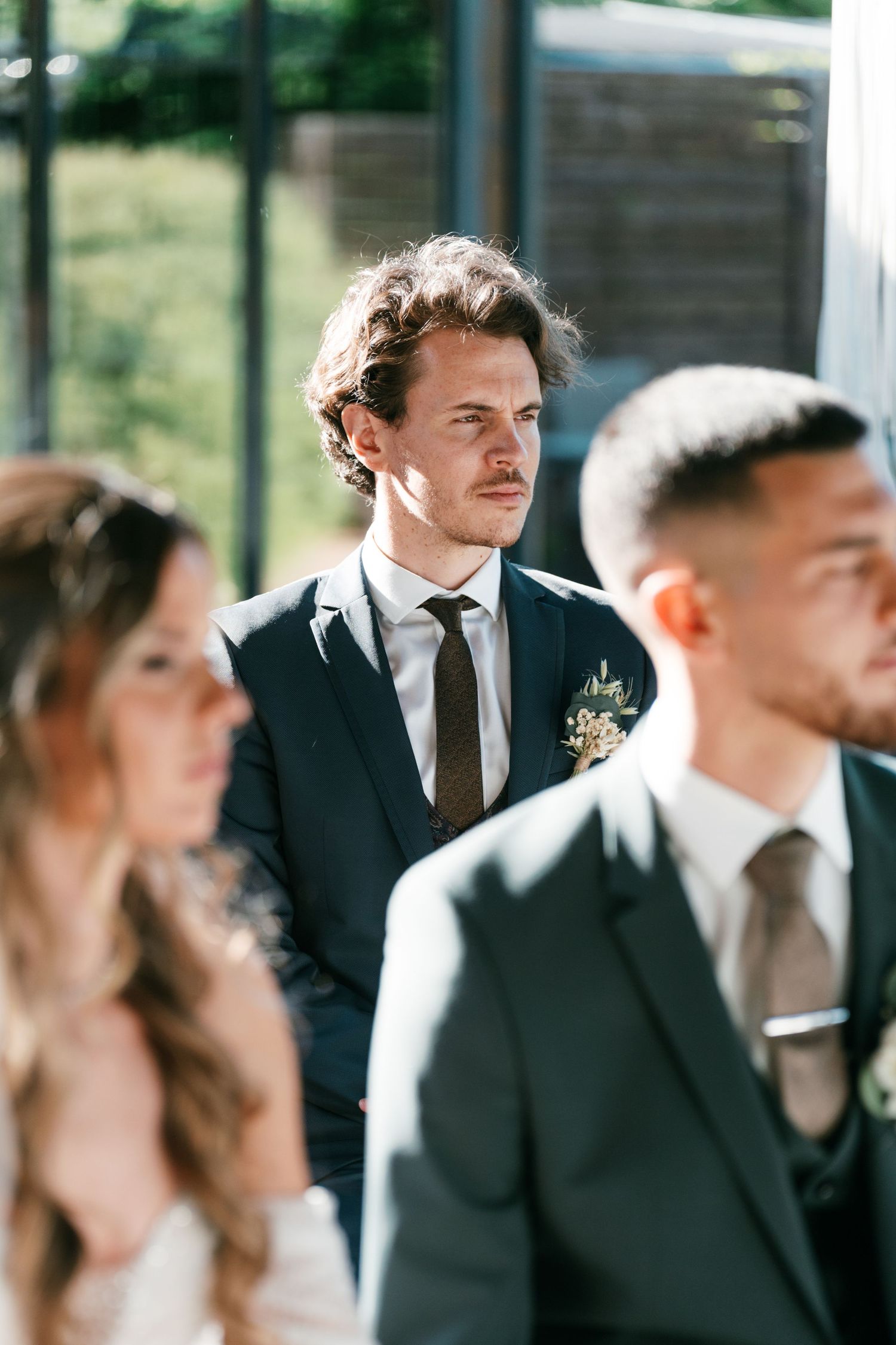 Elegant groomsman in dark suit with boutonniere watching wedding ceremony attentively. Mallorca wedding photographer and filmmaker.