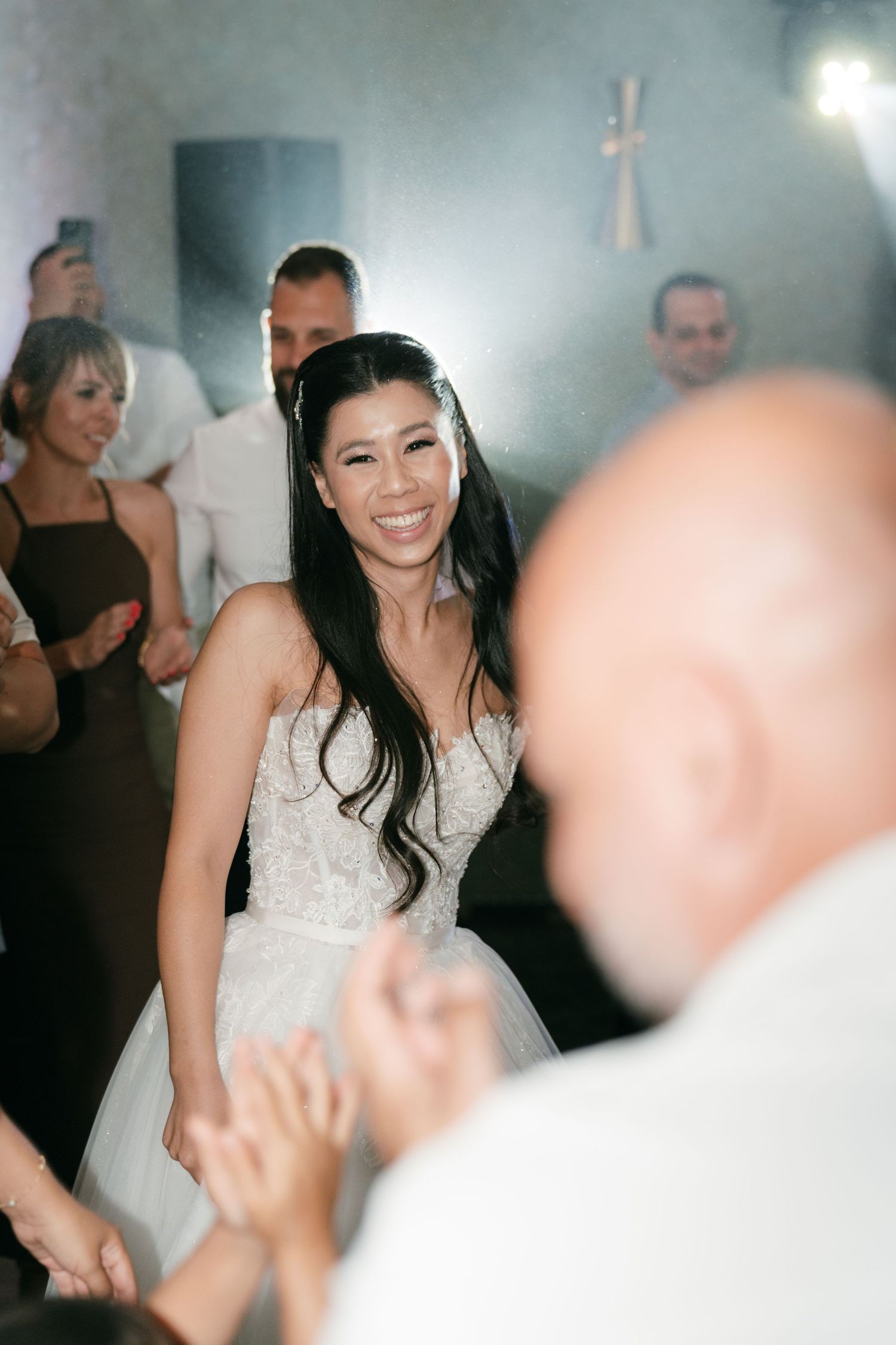 Smiling bride in lace gown dancing joyfully with wedding guests at the reception. Italy wedding photographer and filmmaker