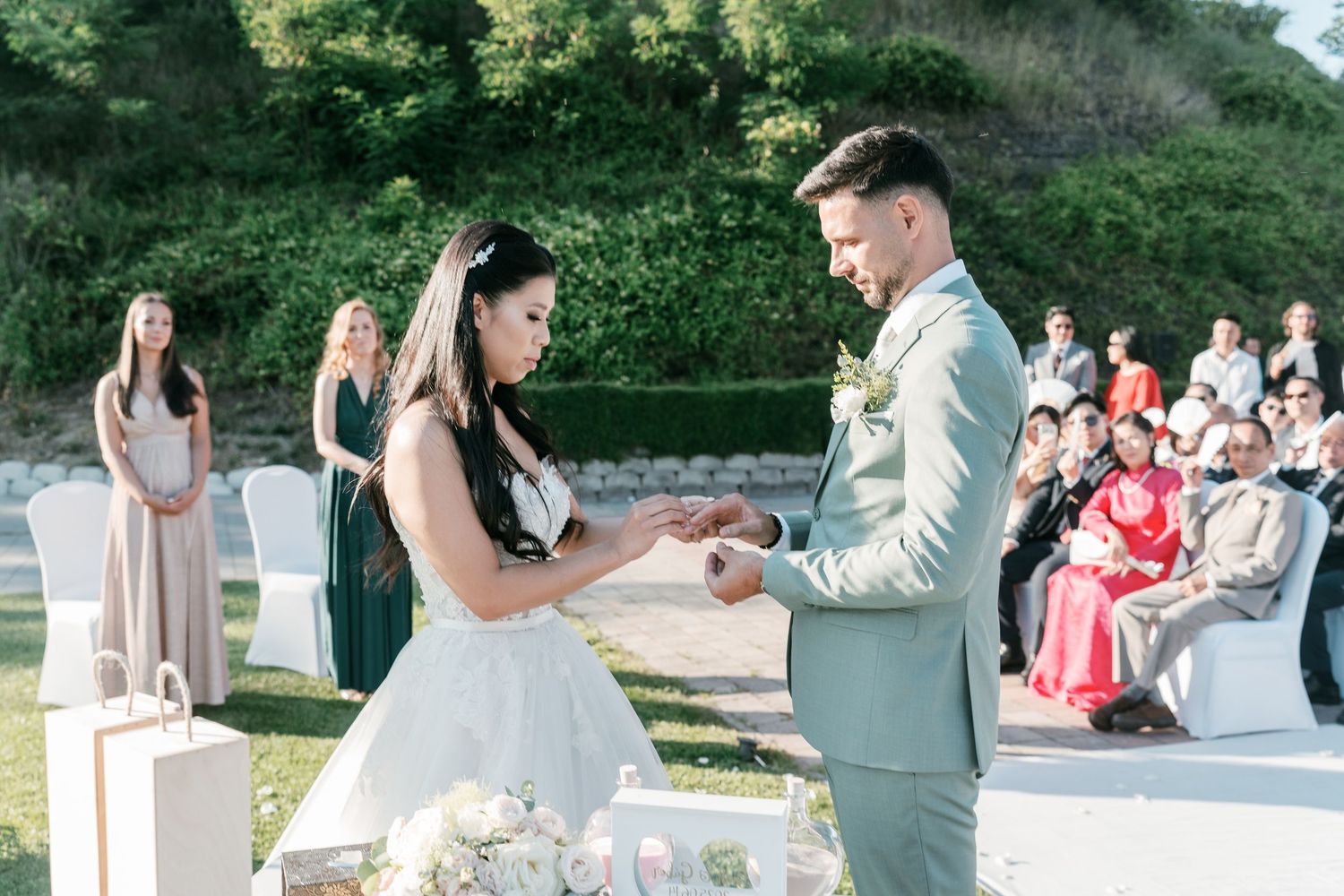 Bride places ring on grooms finger during outdoor wedding ceremony with guests watching. Italy wedding photographer and filmmaker