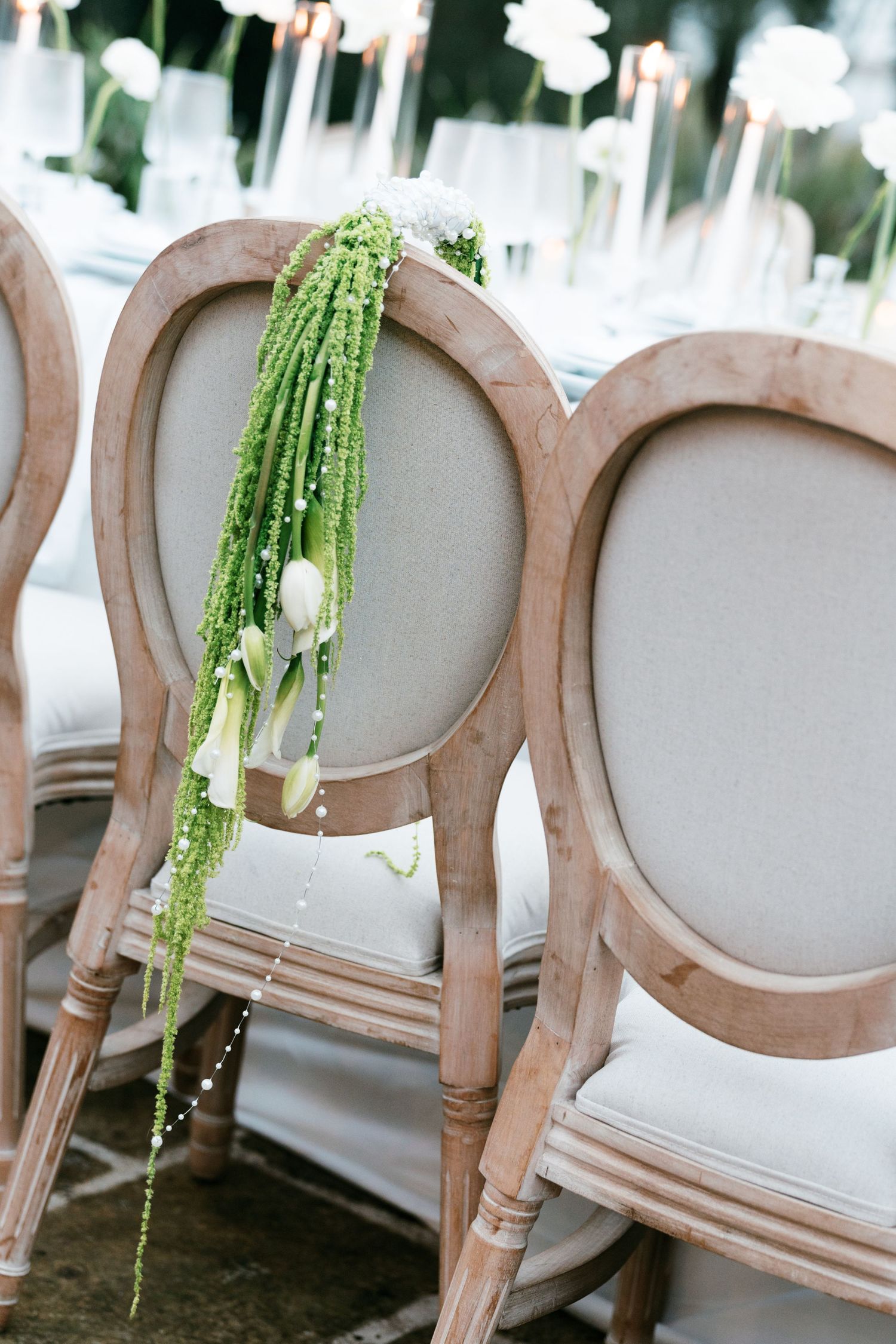 Elegant French-style wooden chairs decorated with cascading green amaranthus and white tulips. Puglia wedding photographer, film