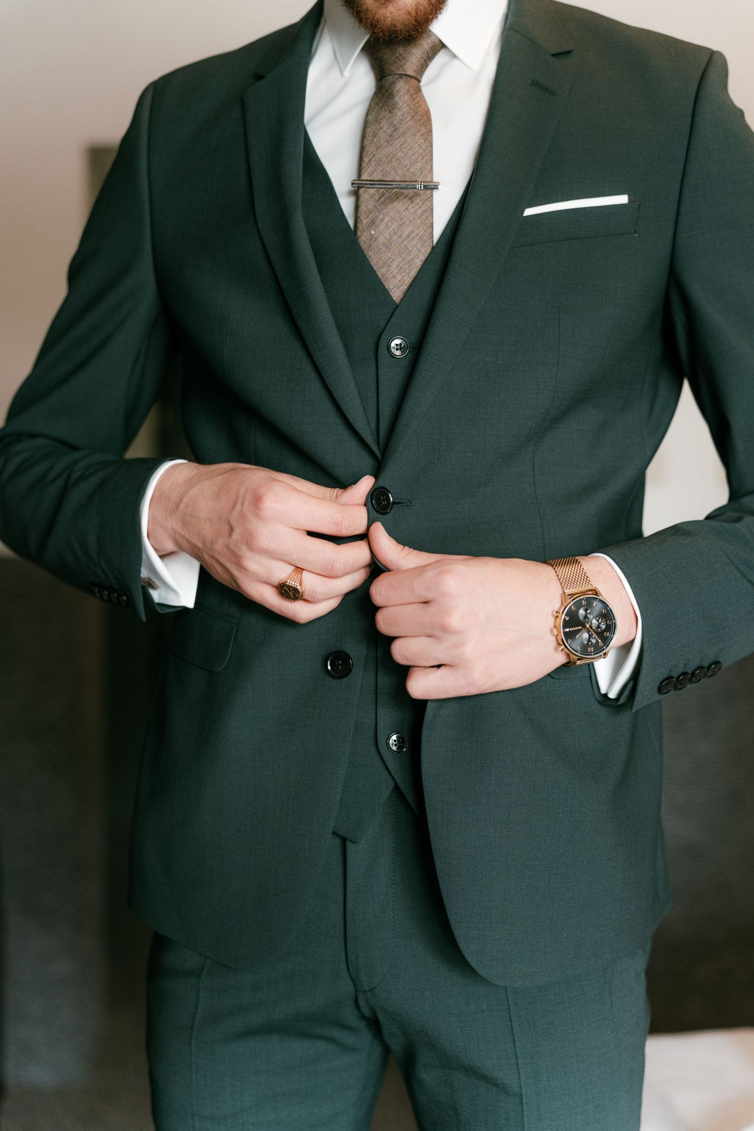 Groom in dark green three-piece suit buttoning jacket with gold watch and ring. Mallorca wedding photographer and filmmaker.
