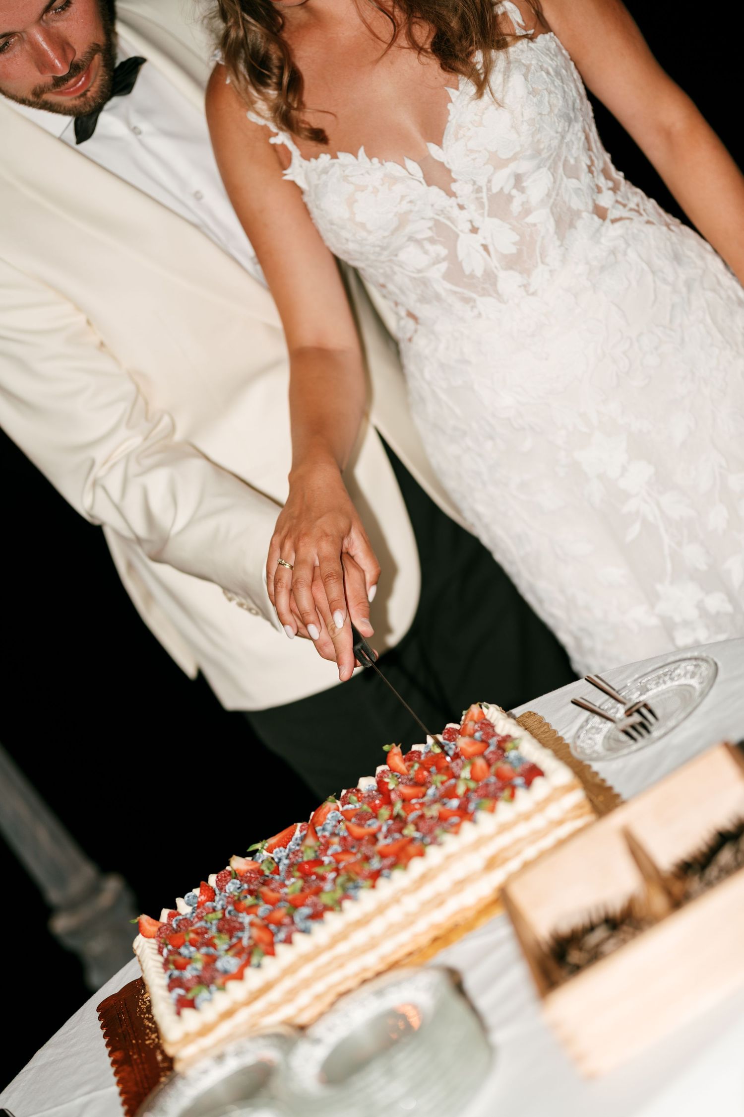 Bride and groom cutting a layered wedding cake topped with fresh strawberries and colorful decorations at their reception.