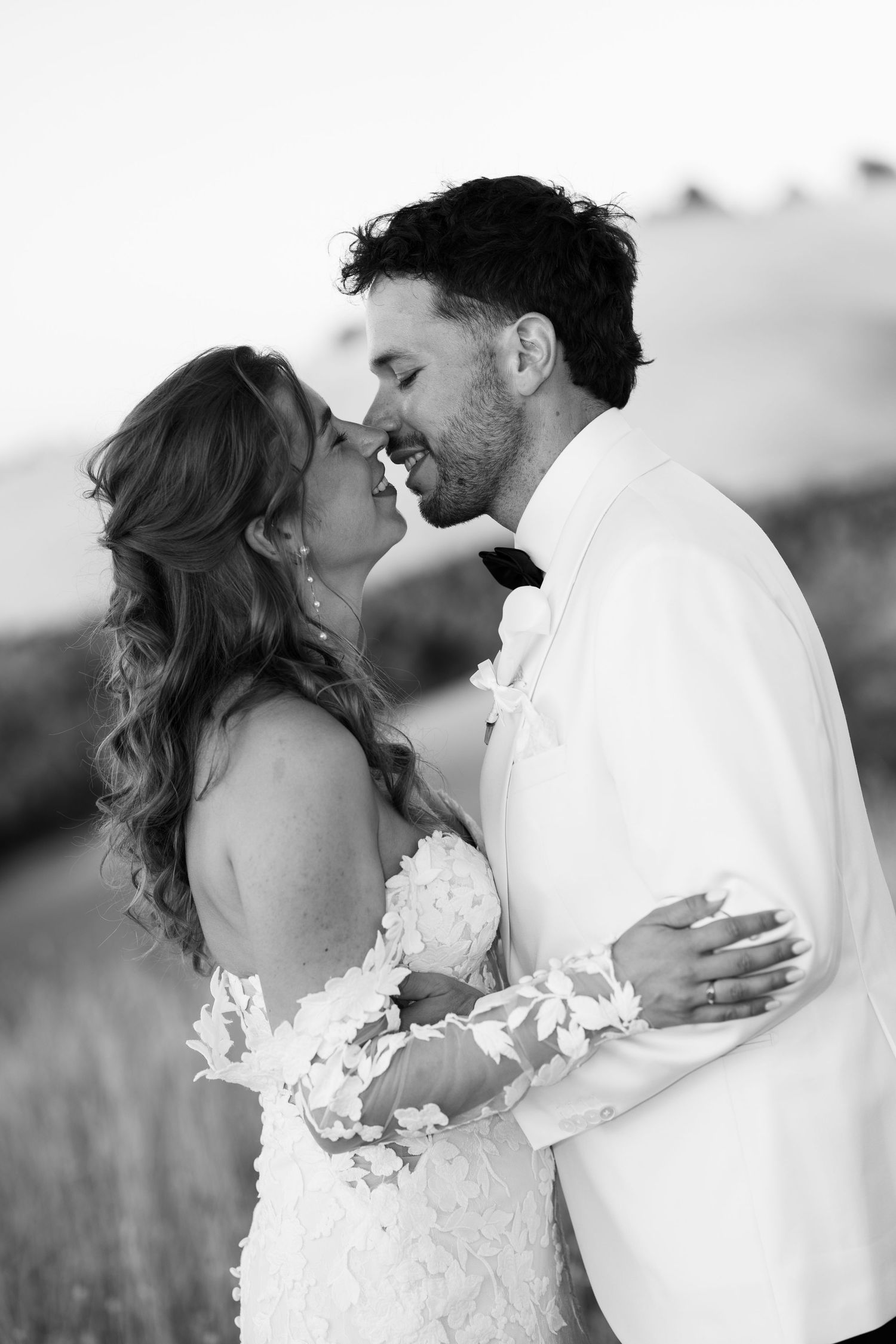 Black and white photo of a bride and groom sharing an intimate moment, nearly kissing outdoors on their wedding day.