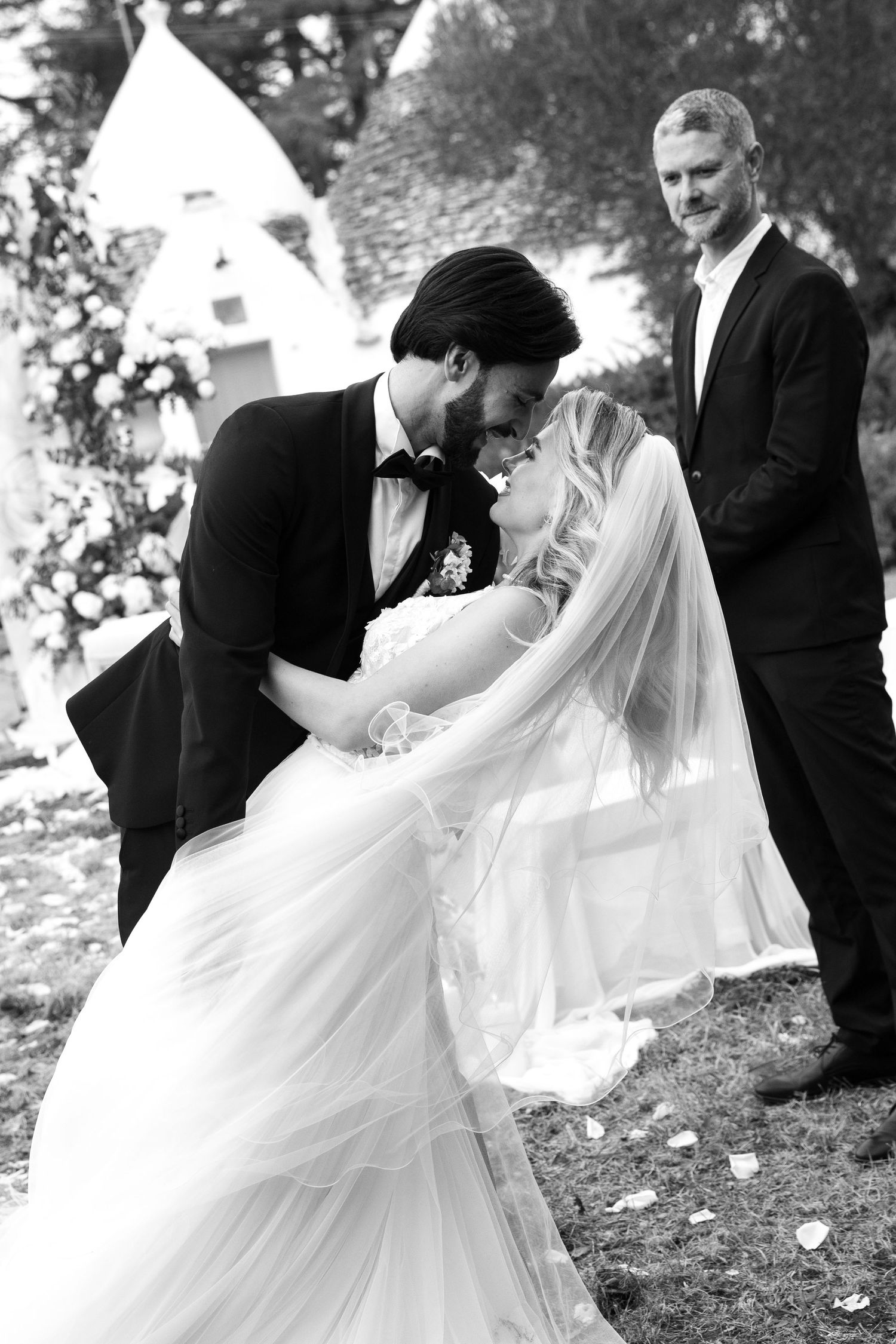 Black and white photo of bride and groom sharing first kiss at outdoor wedding ceremony. Puglia wedding photographer, film