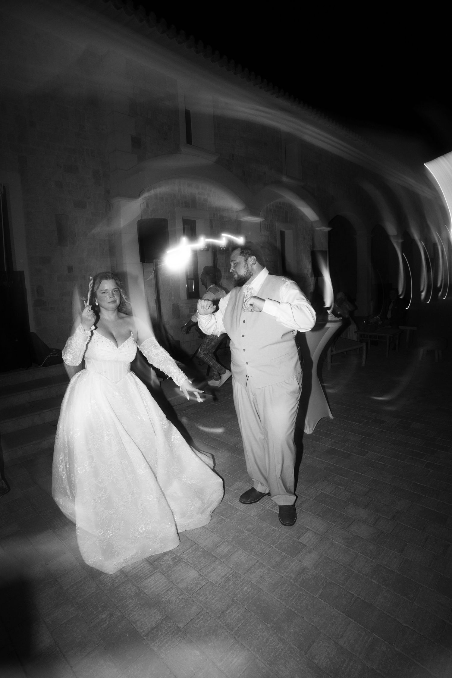 Black and white photo of bride and groom sharing first dance outdoors at night near stone arched venue in Mallorca.