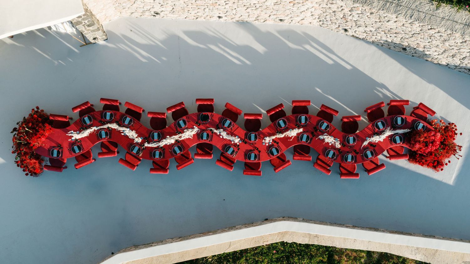 Aerial view of a large group dressed in red forming a decorative pattern on a gray surface outdoors.