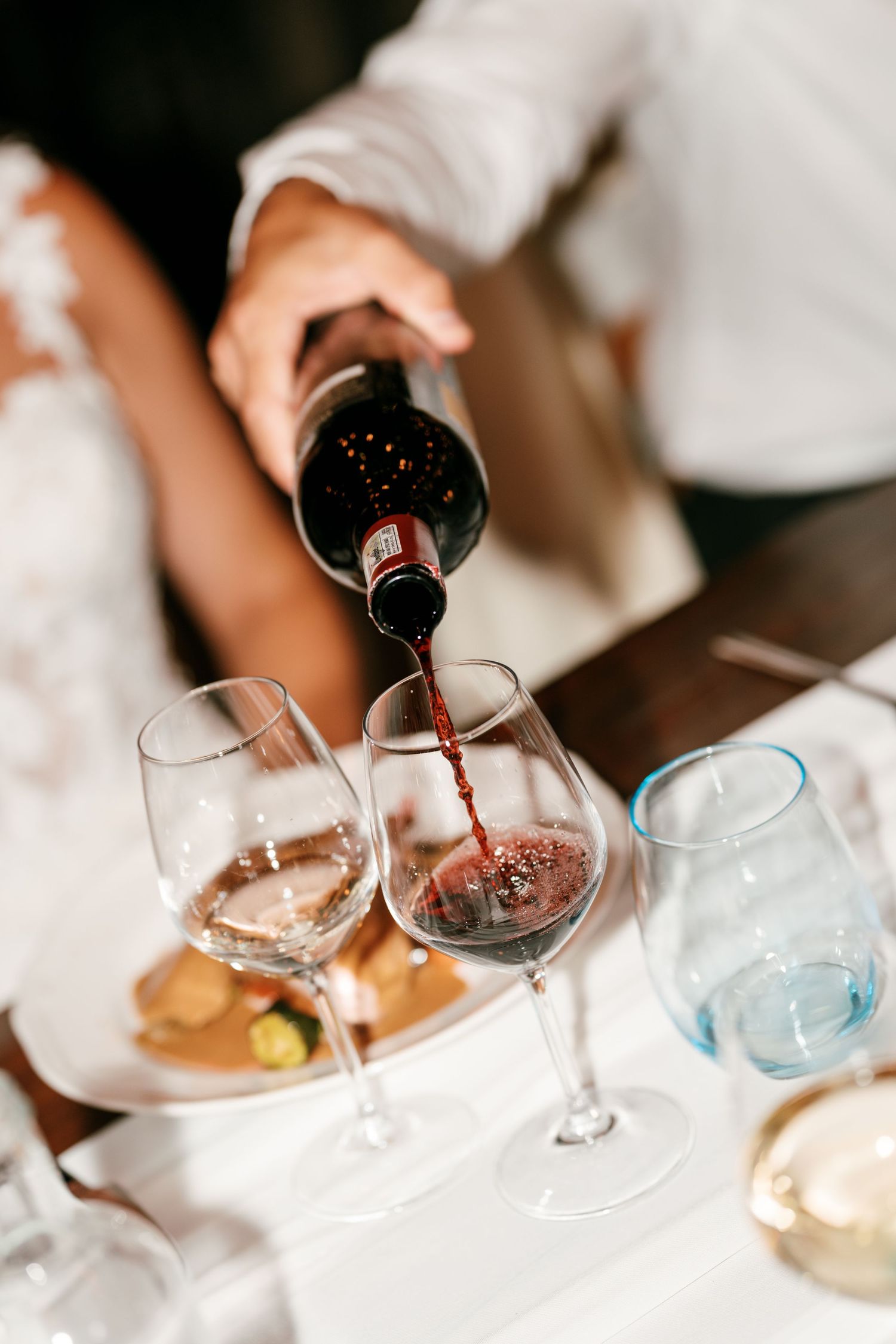 Person pouring red wine into a glass at an elegant dining table with multiple wine glasses.