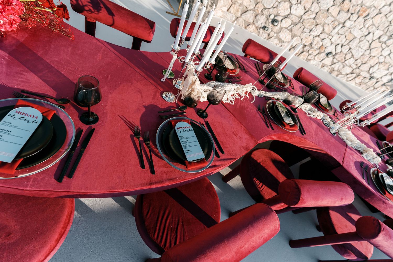Elegant red velvet table setting with black plates, candles, and floral centerpiece for a luxurious event.