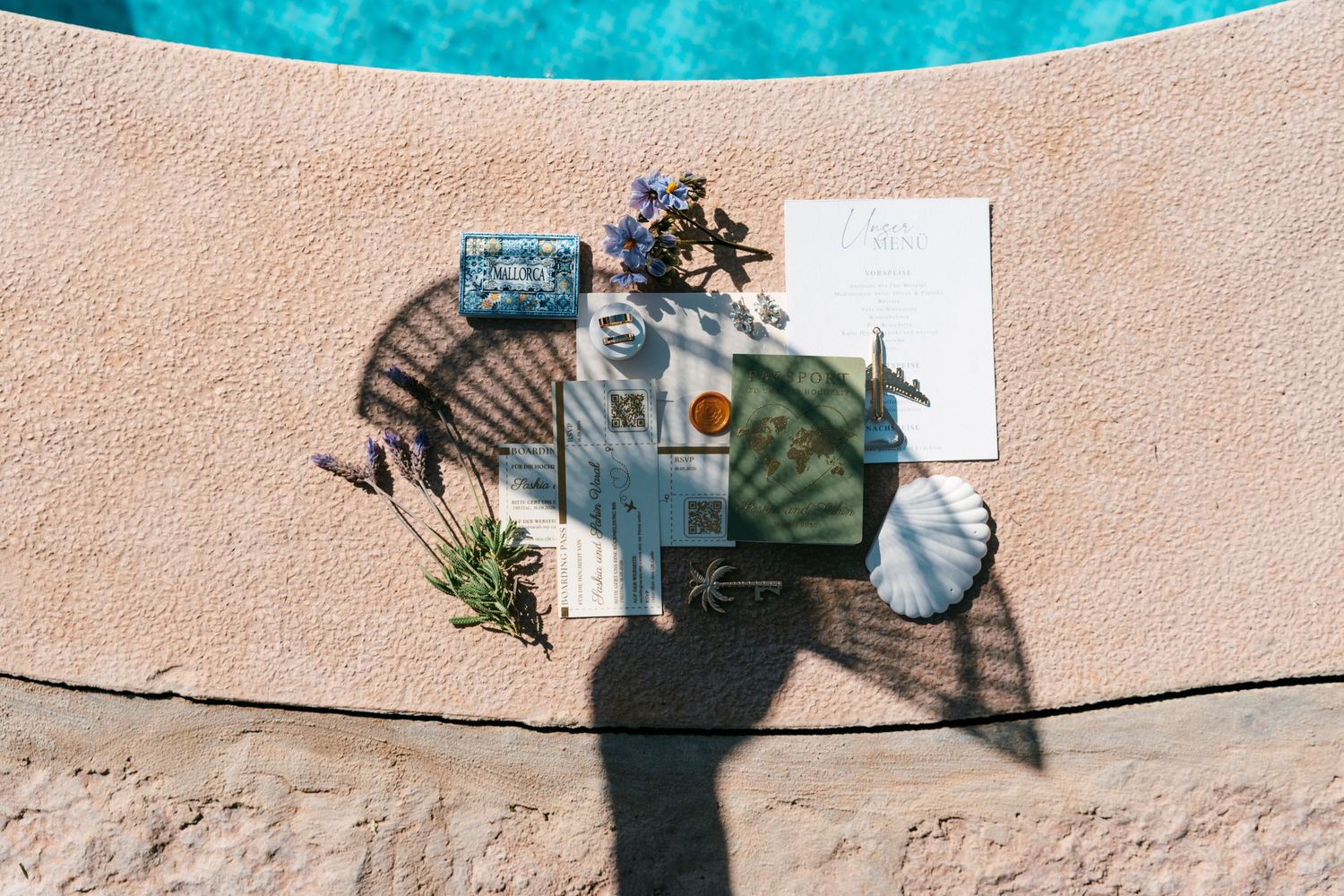 Aerial view of elegant poolside table setting with fan, flowers, and stationery on textured terracotta surface in Mallorca.