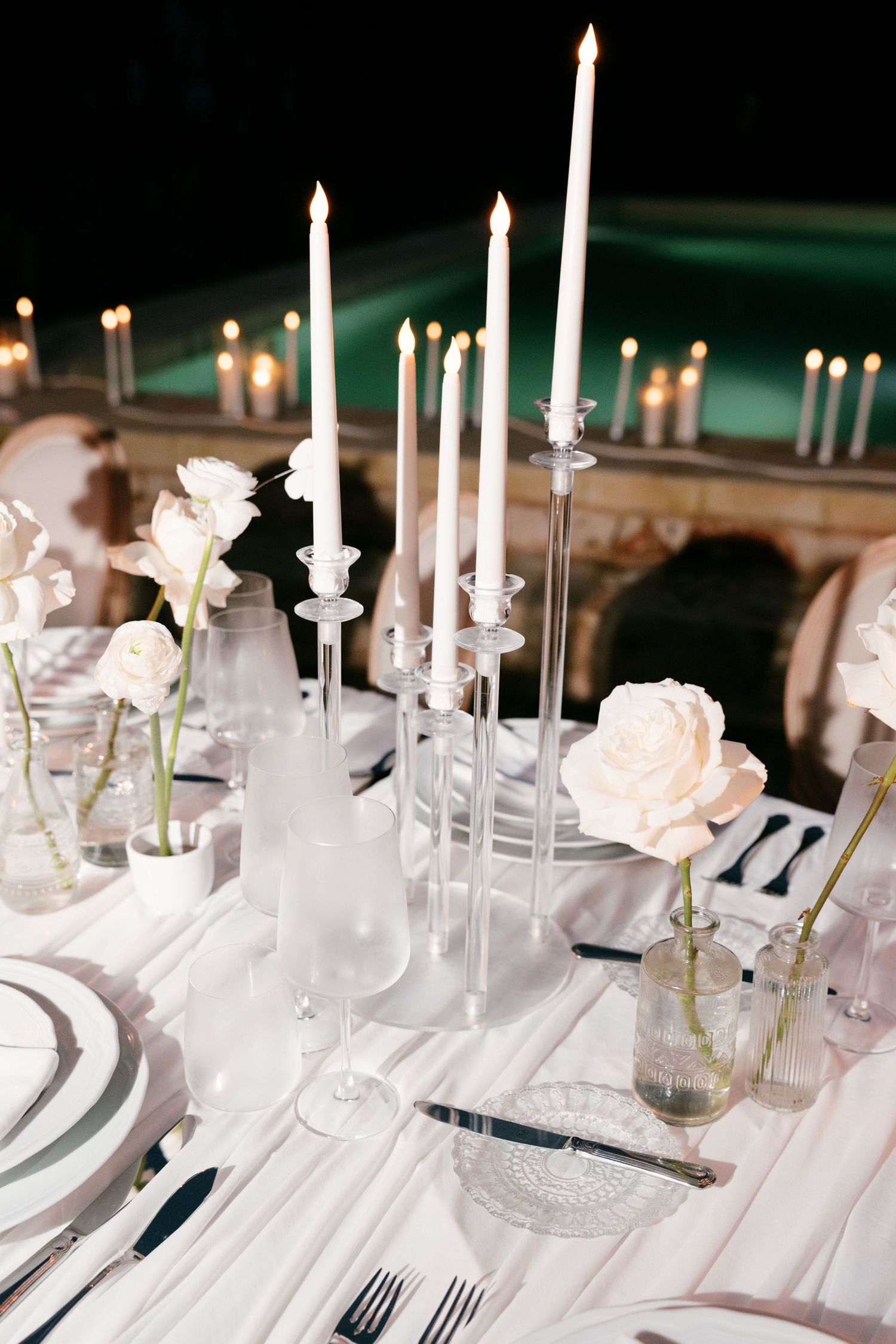 Sophisticated wedding table setting with tall white candles, white roses, and crystal glassware at night. Puglia wedding photographer, film