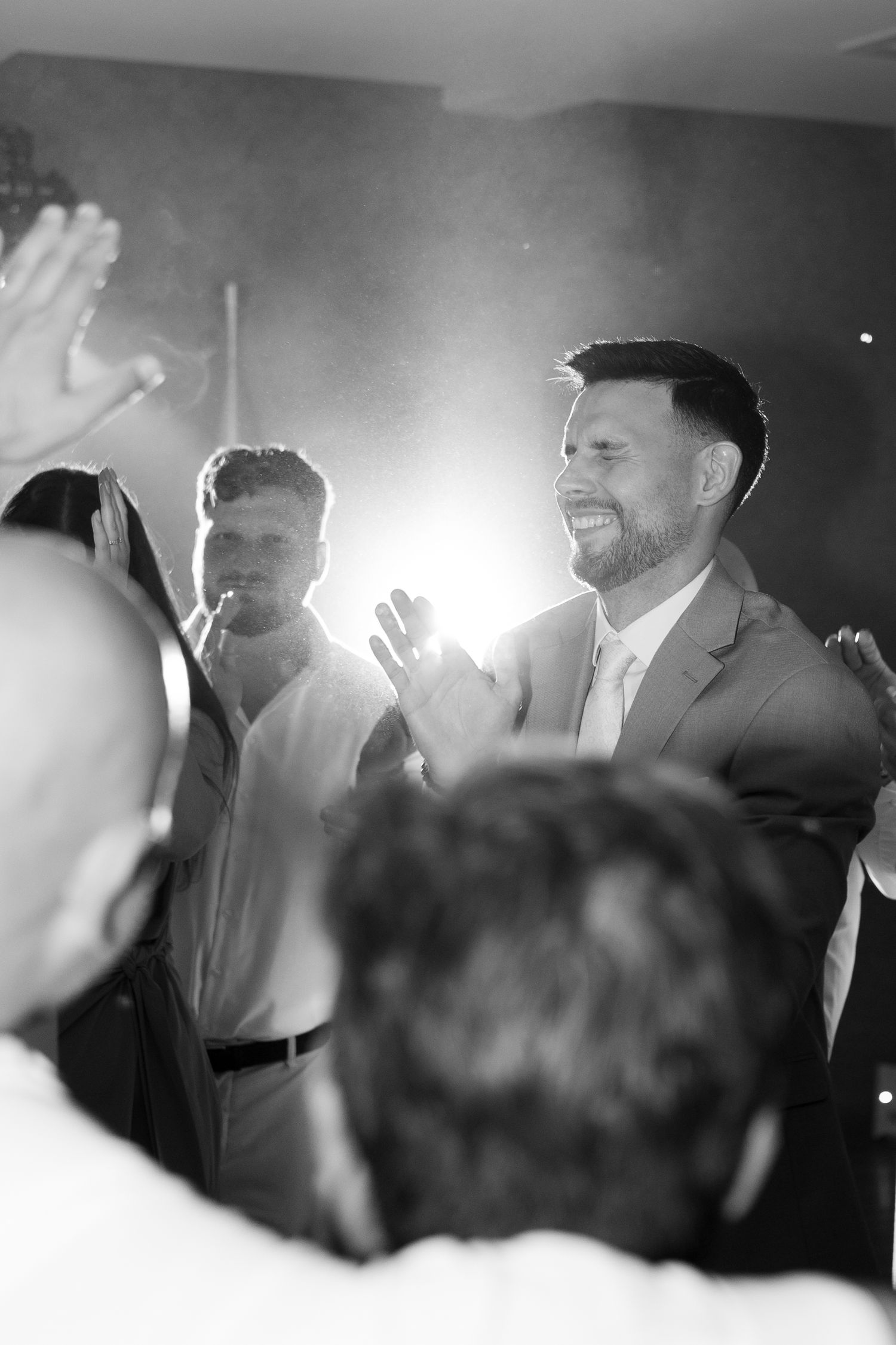 Black and white photo of smiling groomsmen clapping and celebrating at wedding reception. Italy wedding photographer and filmmaker