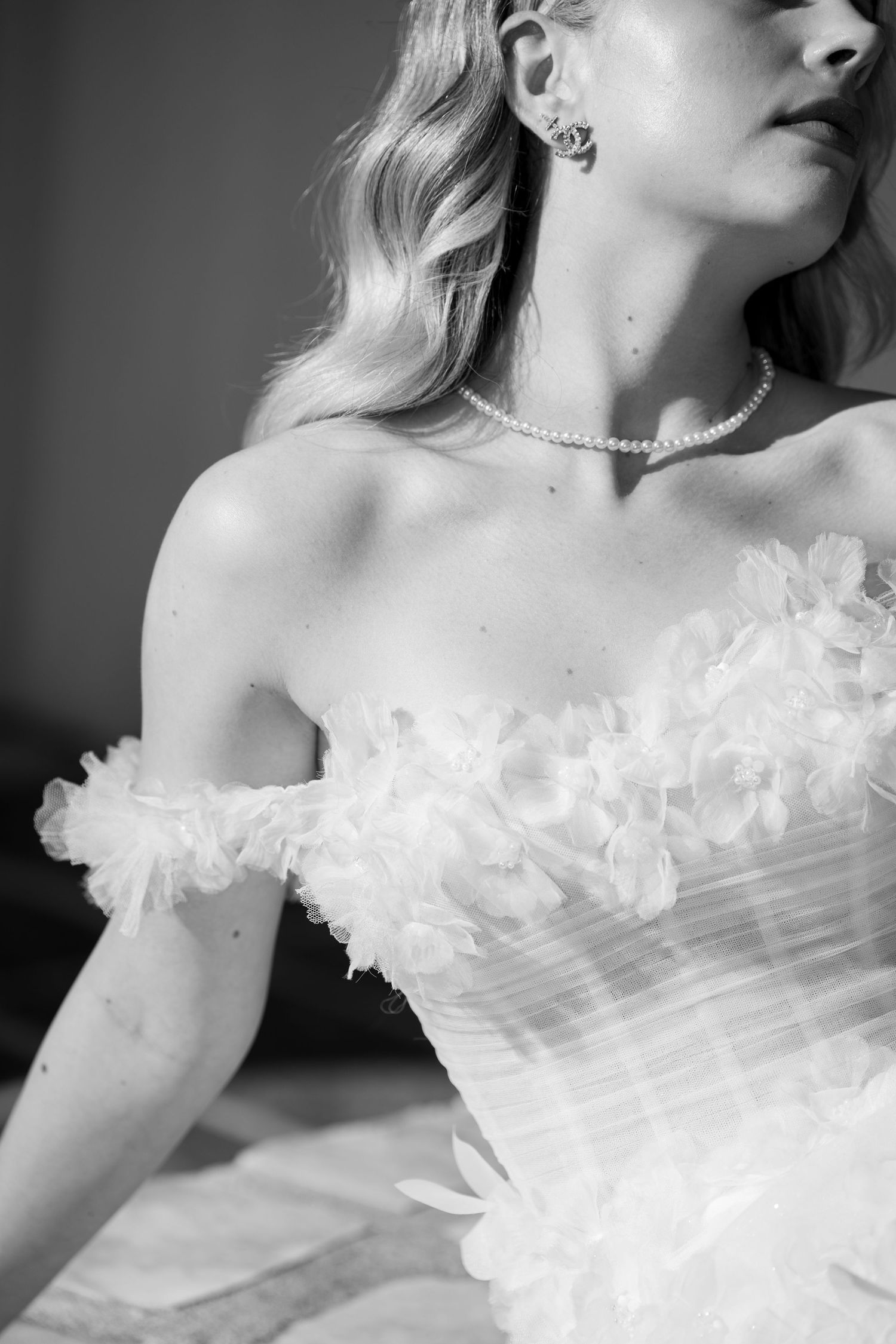 Black and white close-up of a bride in a floral off-shoulder wedding gown wearing a pearl necklace. Mallorca wedding photographer, filmmaker