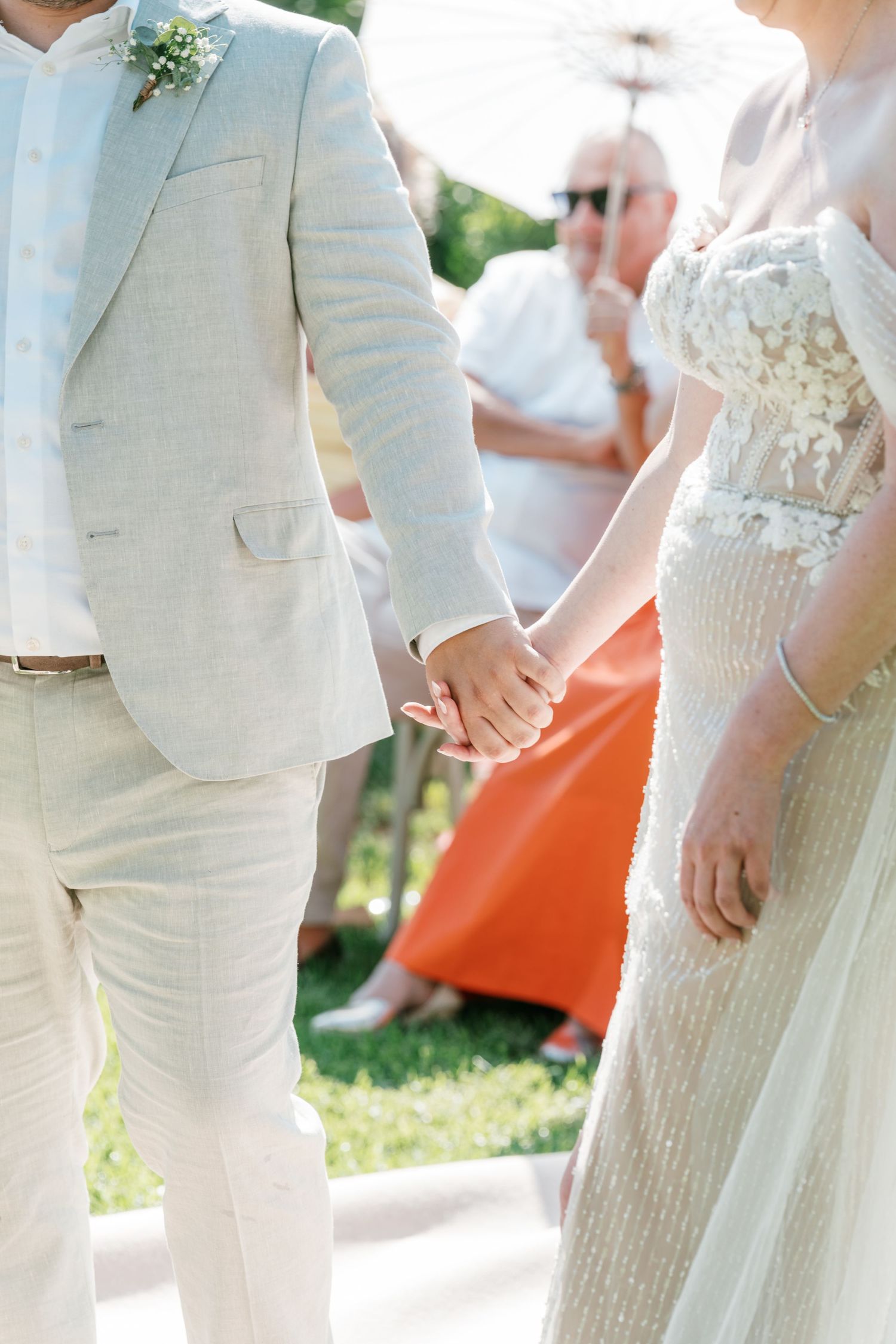 Bride and groom holding hands at outdoor wedding ceremony, groom in beige linen suit, bride in lace gown. Mallorca wedding photographer
