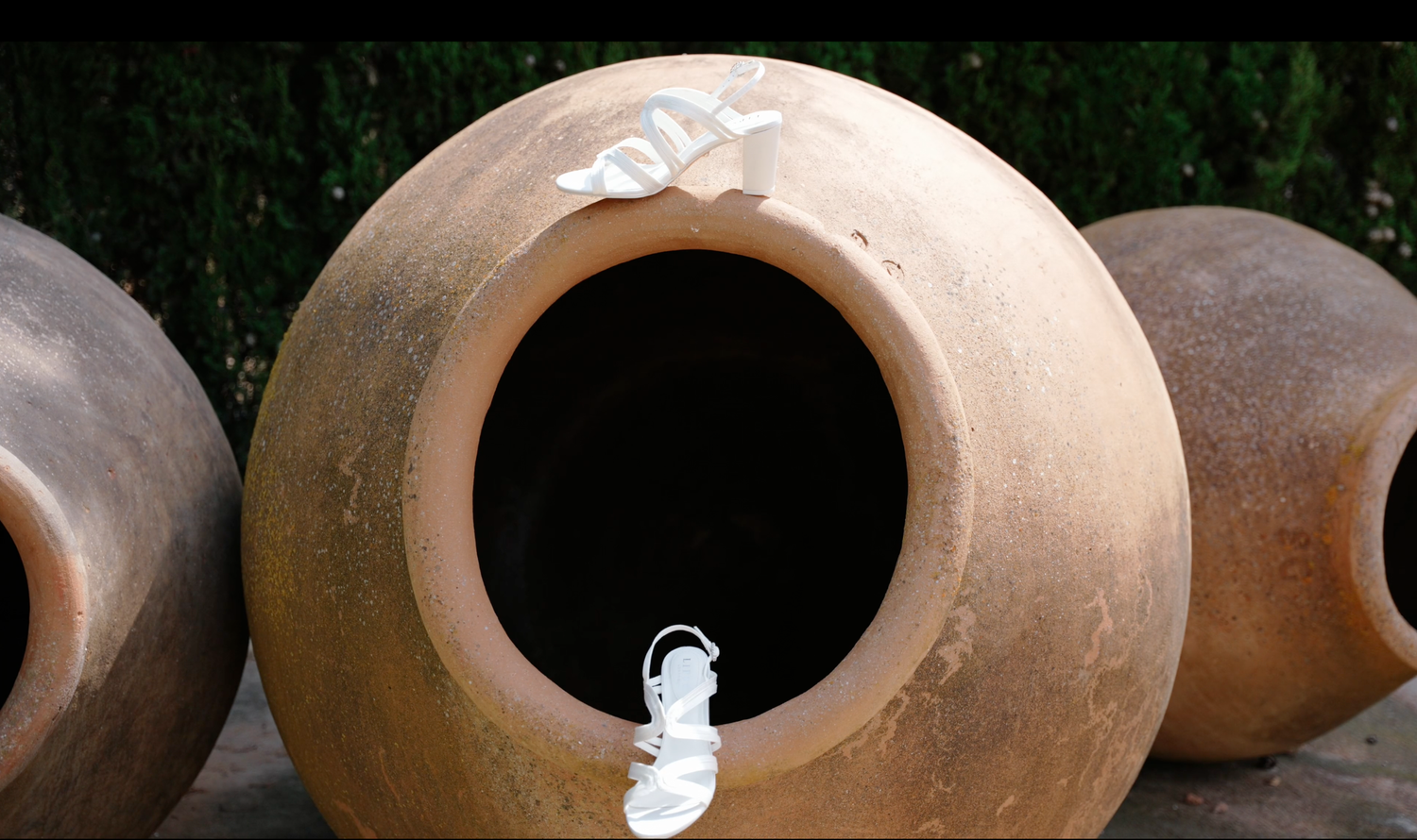 Large terracotta clay pot with a wide round opening and white fabric ties, with similar earthenware jars blurred in the background.