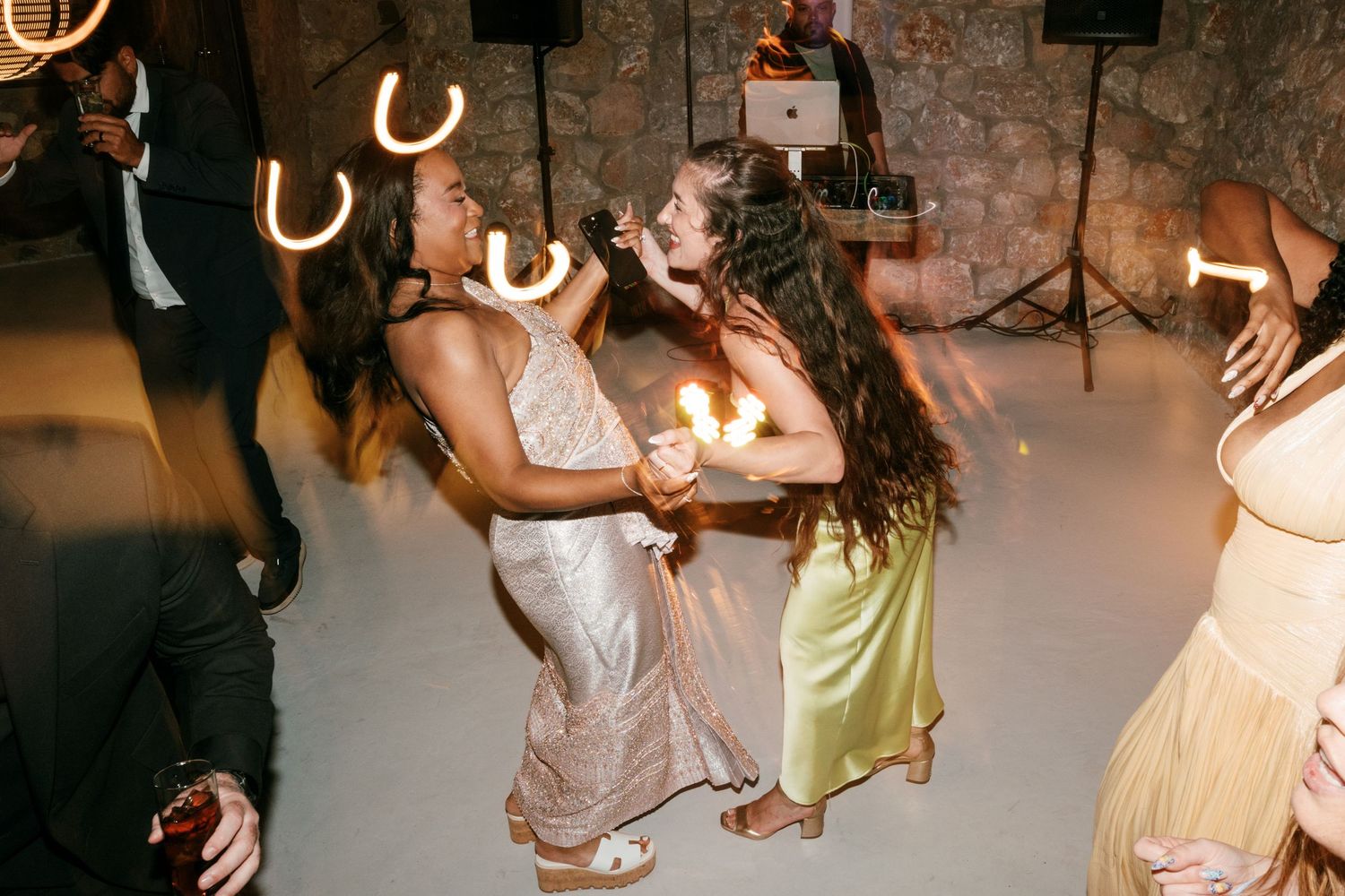 Women dancing joyfully at a wedding reception with sparklers and glowing lights on the dance floor.