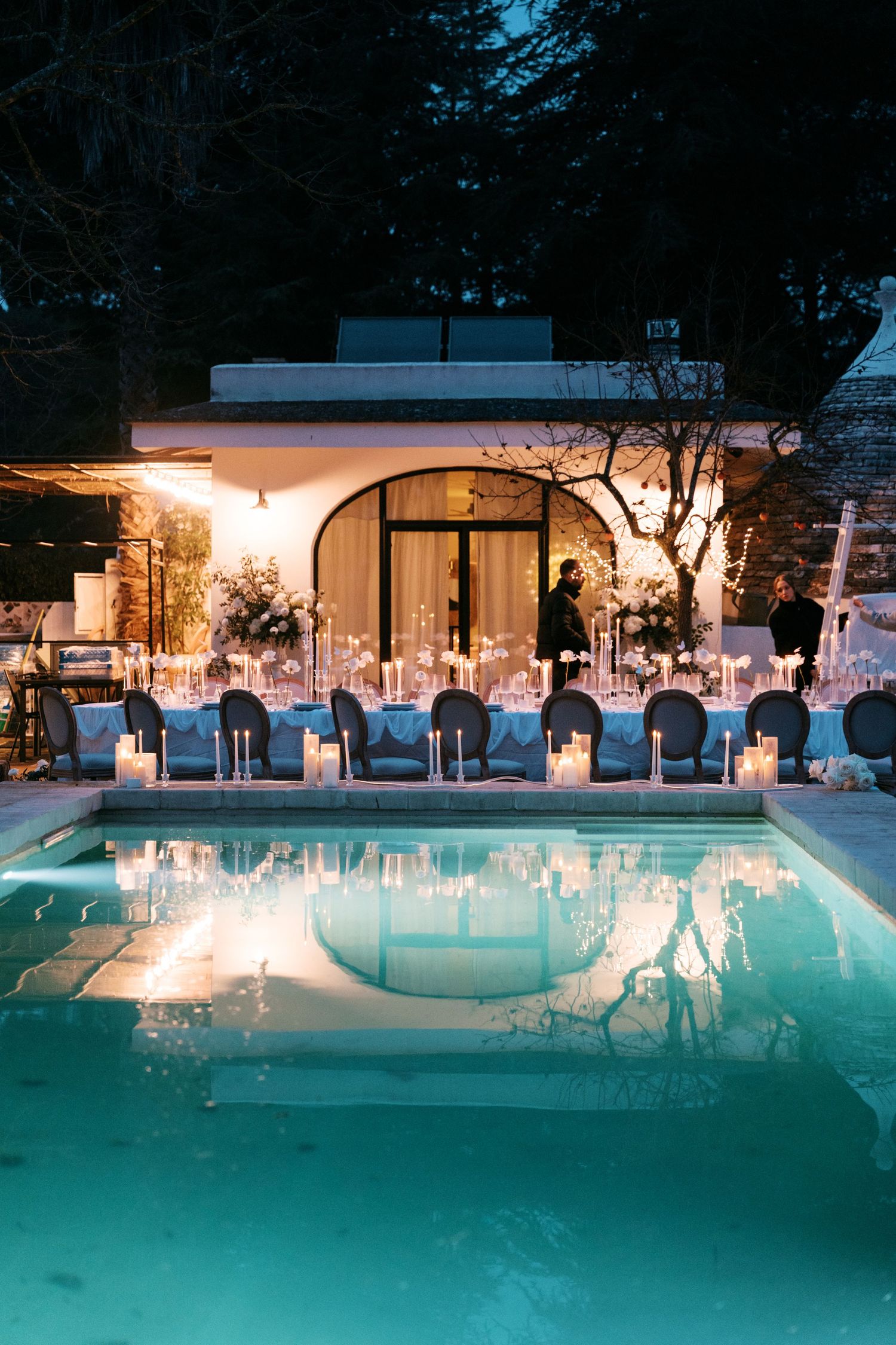 Nighttime outdoor wedding reception table with candles reflected in a glowing turquoise pool. Mallorca wedding photographer, filmmaker