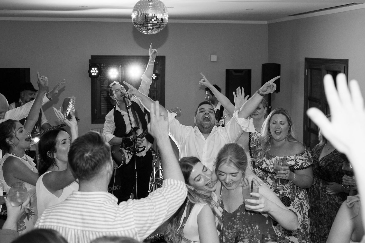 Excited wedding guests dancing under disco ball with hands raised at lively black and white reception. Tuscany wedding photographer, filmmak