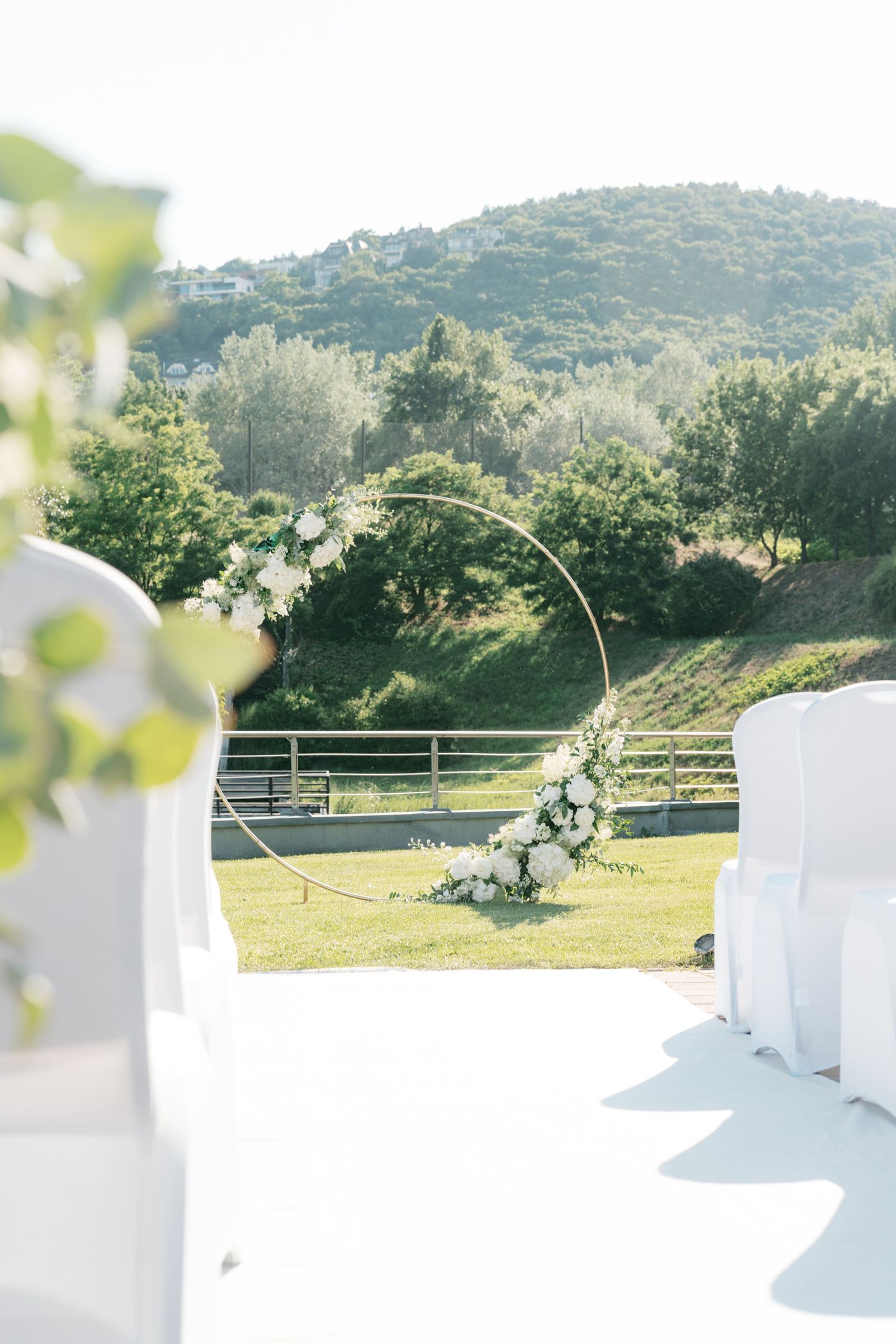 Circular gold wedding arch with white flowers set against scenic mountain backdrop outdoors. Italy wedding photographer and filmmaker