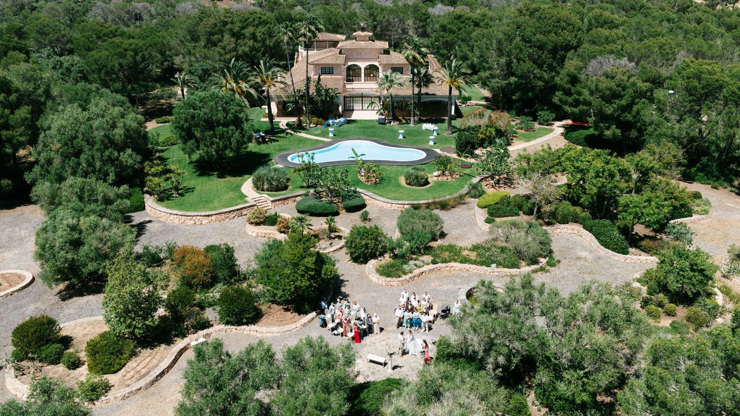 Aerial view of a luxurious Mediterranean villa with a pool, manicured gardens, and lush greenery surrounding the estate in Mallorca.