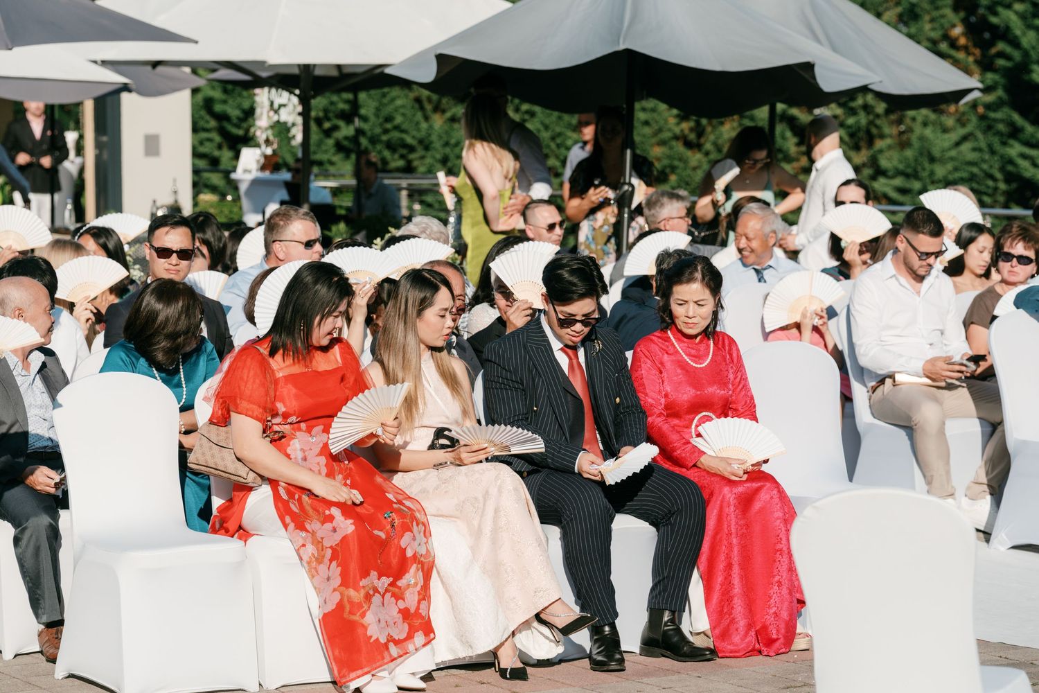 Wedding guests seated outdoors under umbrellas, wearing traditional Vietnamese ao dai attire. Italy wedding photographer and filmmaker
