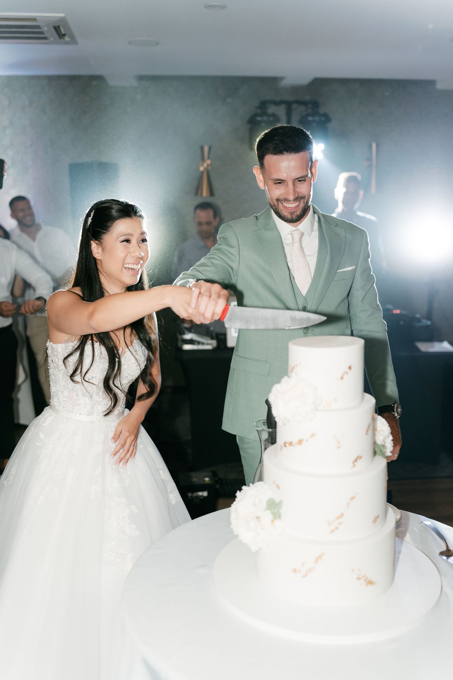 Smiling bride and groom cutting their elegant four-tier white wedding cake together. Italy wedding photographer and filmmaker