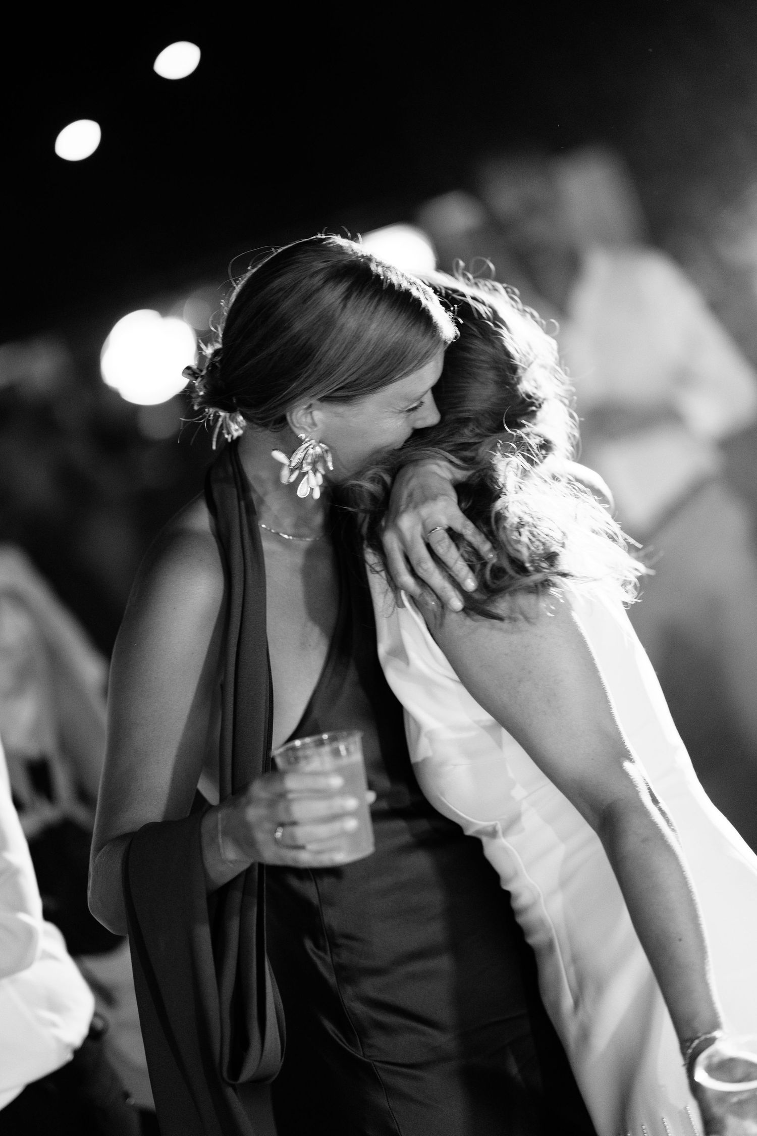 Two women sharing an emotional hug on the dance floor at a wedding reception in black and white.