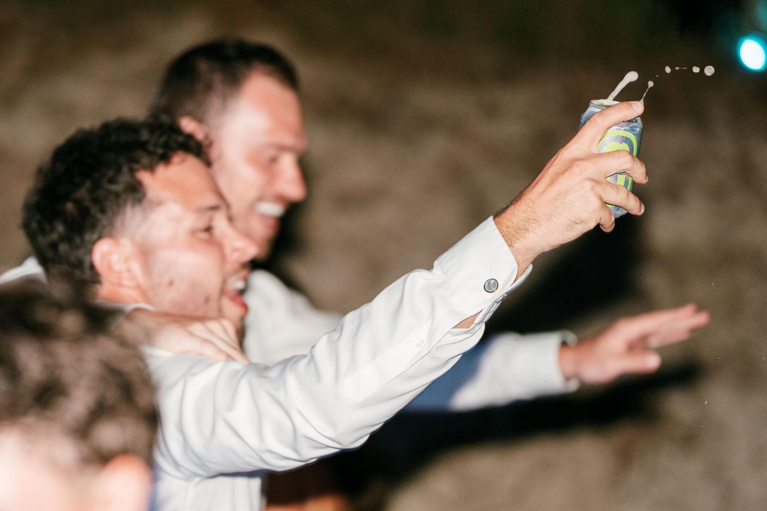 Man in white shirt raises a drink can in celebration at a lively party event.