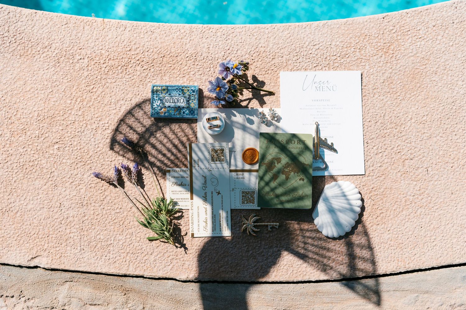 Aerial view of poolside decor with fan, book, flowers, and accessories on a textured pink surface.