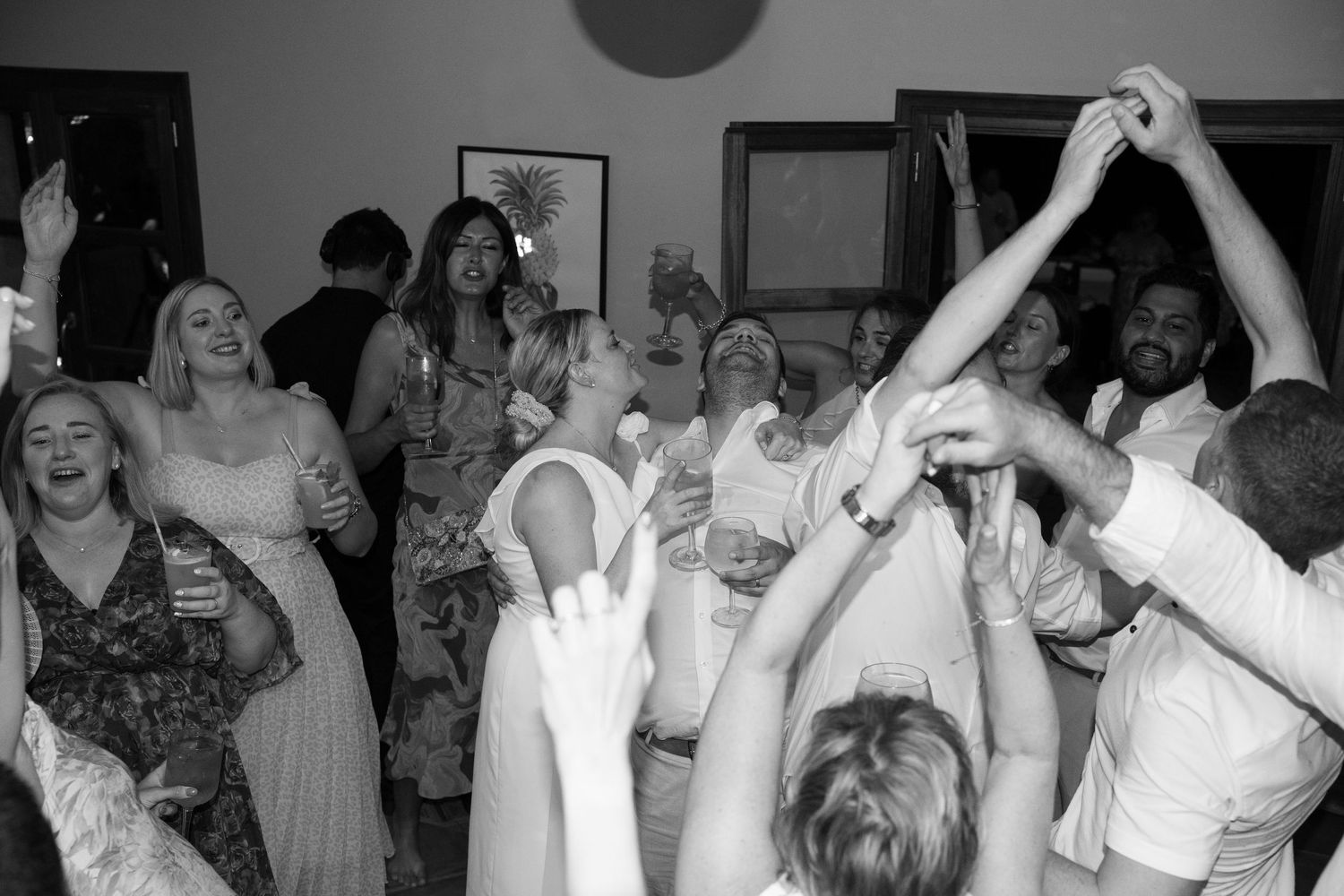 Energetic black and white photo of wedding guests dancing with hands raised at reception party. Puglia wedding photographer,