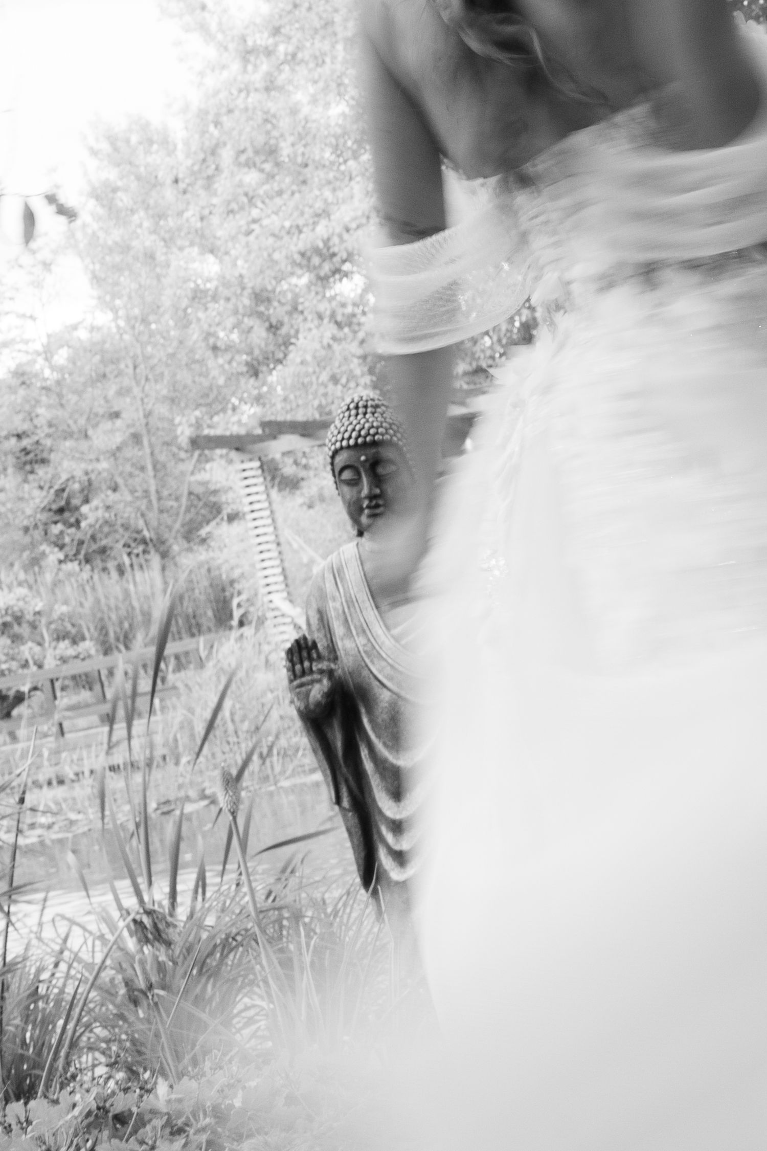 Black and white artistic photo of bride in white gown beside Buddha statue in garden. Mallorca wedding photographer and filmmaker.