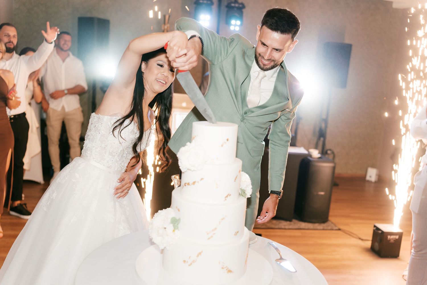 Bride and groom cut a tall white wedding cake surrounded by sparkling fireworks at their reception. Italy wedding photographer and filmmaker