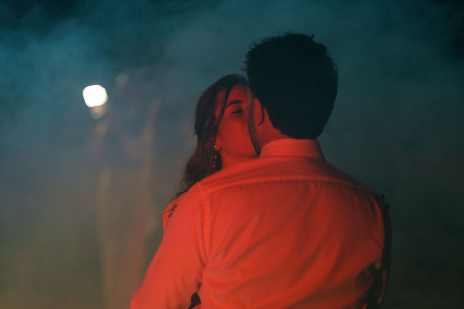 Couple embracing romantically in dramatic red-lit smoky atmosphere at night, viewed from behind.