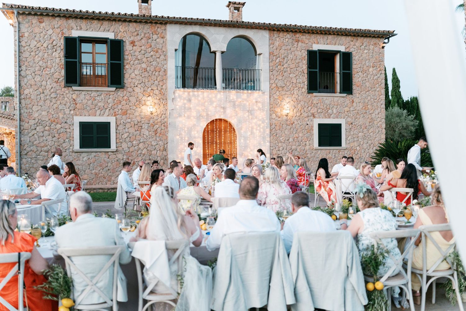Wedding guests dine at an elegant outdoor reception in front of a beautiful stone villa. Tuscany wedding photographer, filmmaker