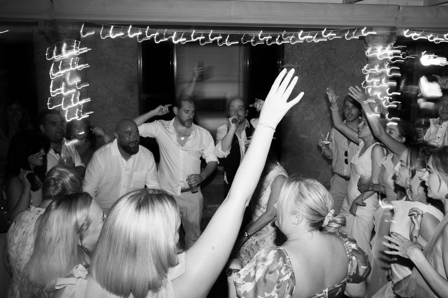 Energetic wedding guests dance under neon lights at a lively indoor wedding reception party. Tuscany wedding photographer, filmmaker