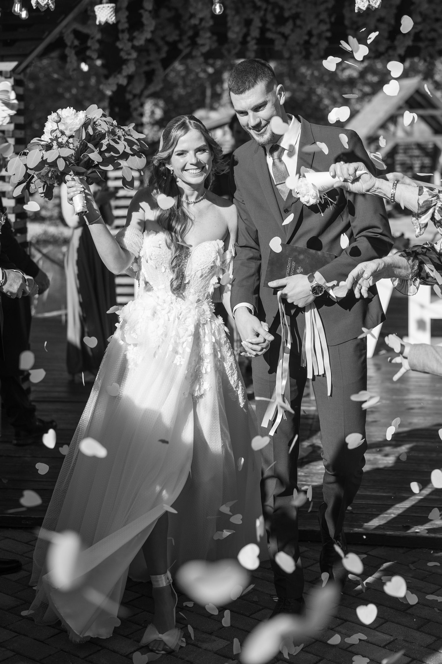 Black and white photo of smiling newlyweds walking through confetti shower after ceremony. Mallorca wedding photographer and filmmaker.