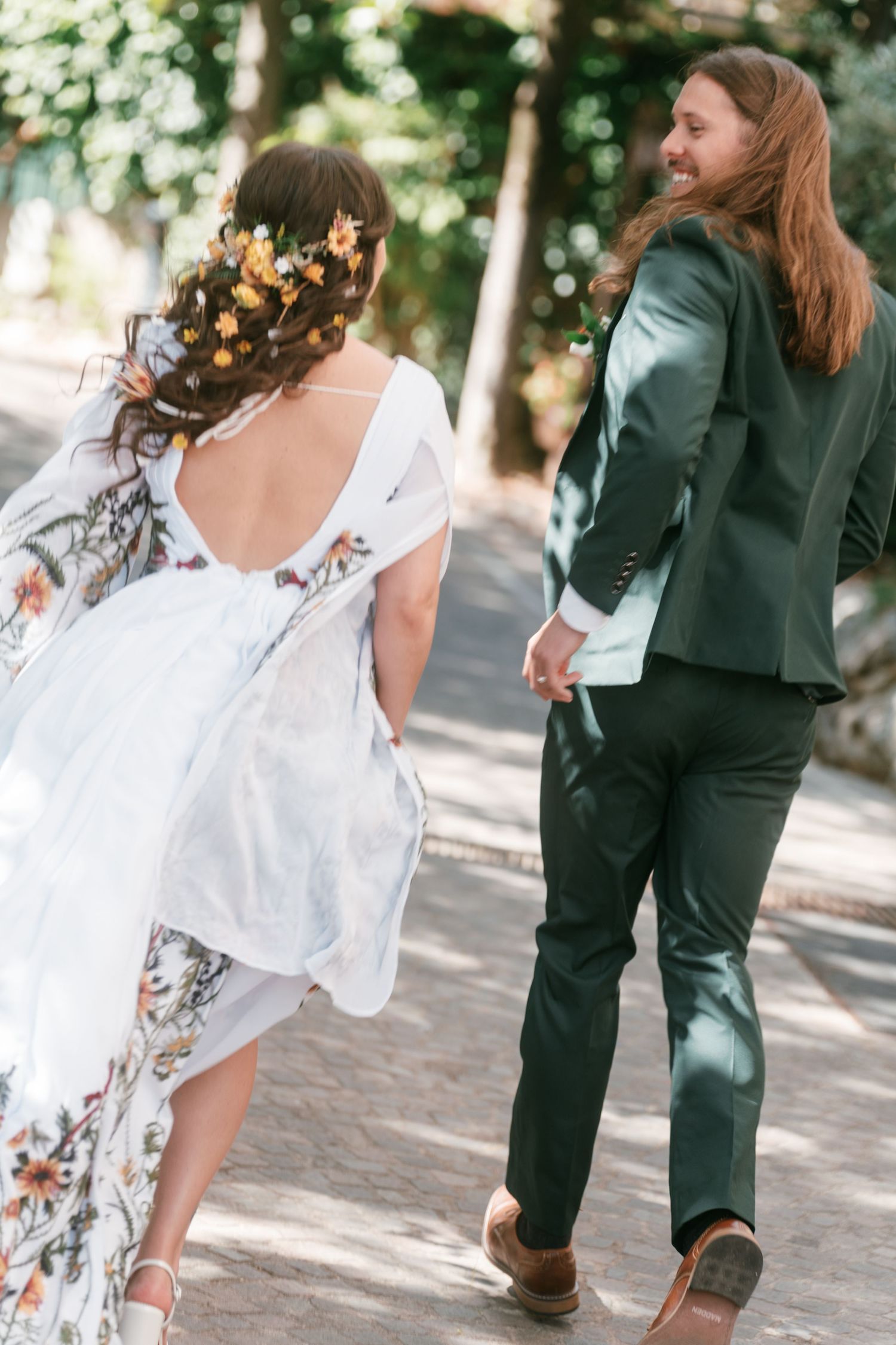 Bride and groom walking hand in hand on sunny path, bride in floral wedding dress. Tuscany wedding photographer, filmmaker