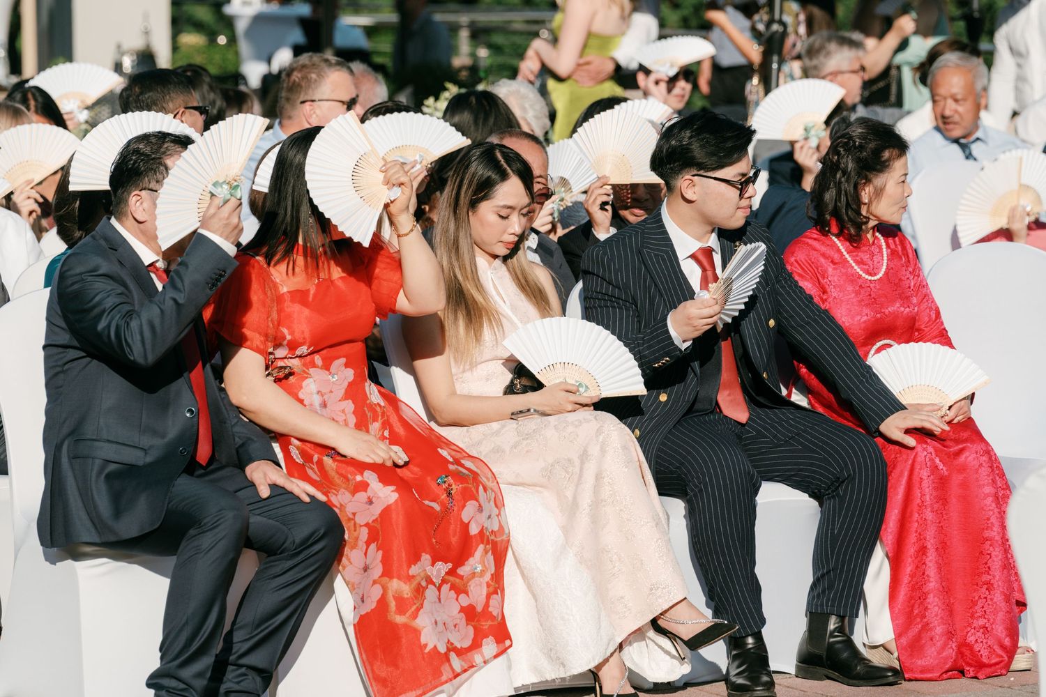 Wedding guests use white hand fans to stay cool during outdoor daytime ceremony. Italy wedding photographer and filmmaker