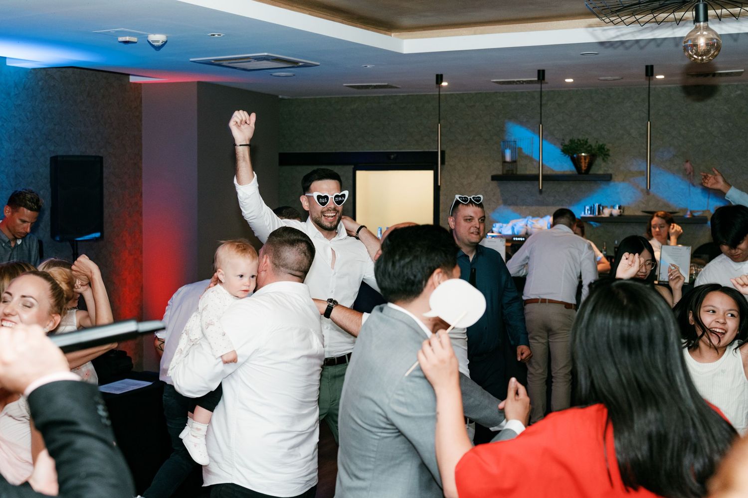 Energetic wedding reception dance floor with guests celebrating and man holding baby. Italy wedding photographer